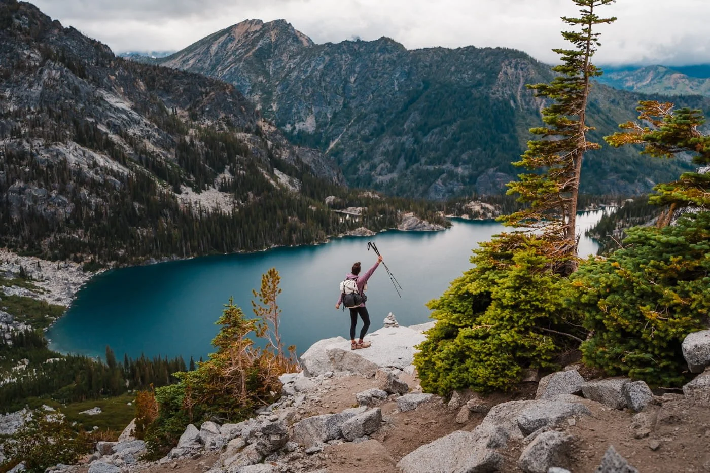 A hiker standing on a rock on aasgard pass overlooking a blue colchuck lake