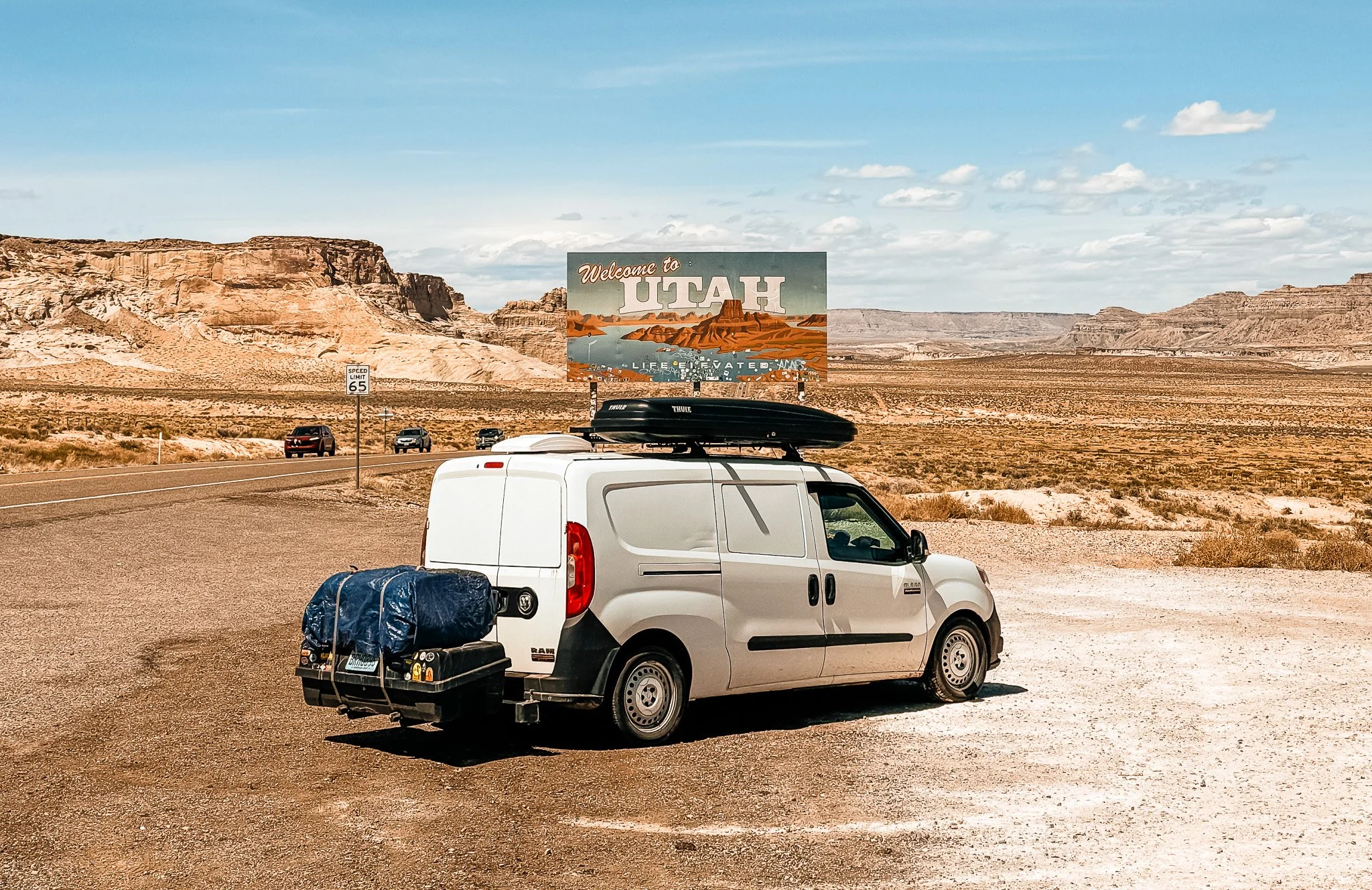 a small white camper van in front of the "welcome to utah" sign in the desert