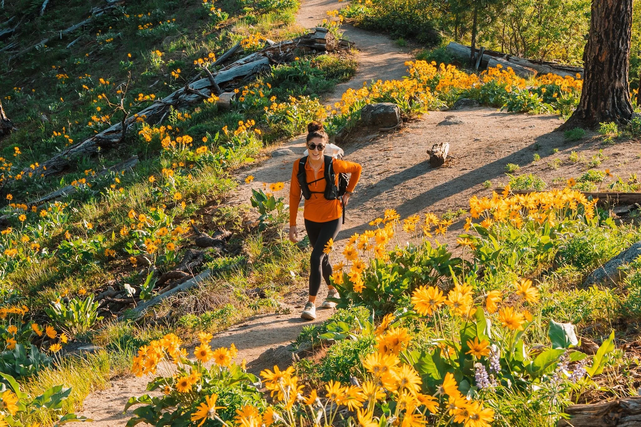 a woman hiking through yellow wild flowers, wearing an orange quarter zip fleece and black leggings