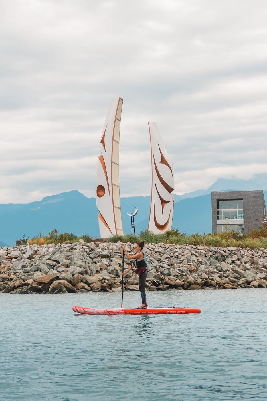 girl on a stand-up paddleboard in front of the Sp’akw’us Feather Park welcome gate