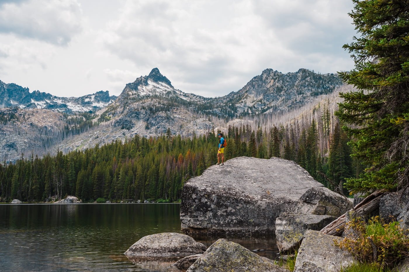 man standing on a boulder along the short of lake stuart in the enchantments