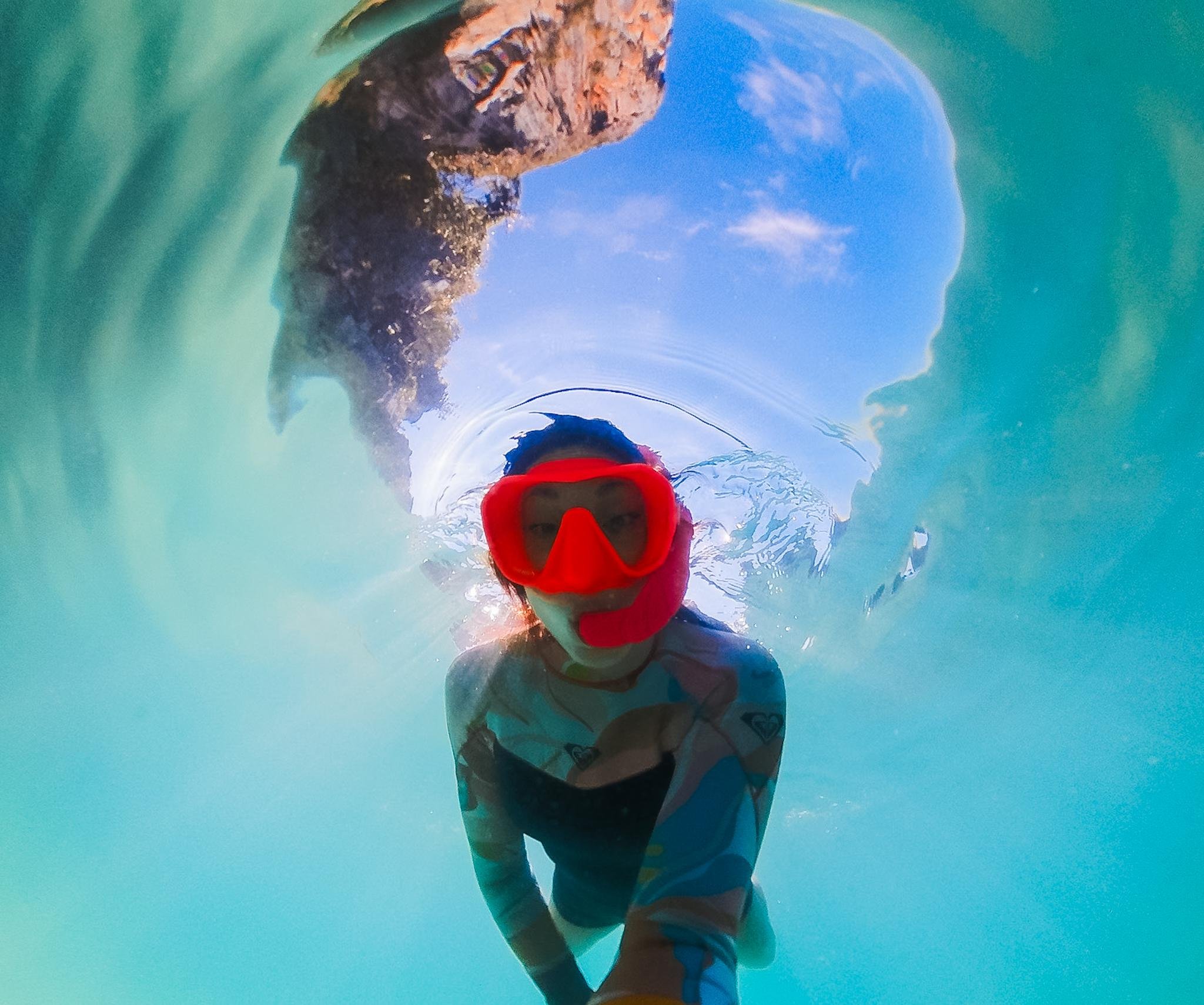 a person snorkeling just under the water, wearing a colorful wetsuit and pright pink mask and snorkel