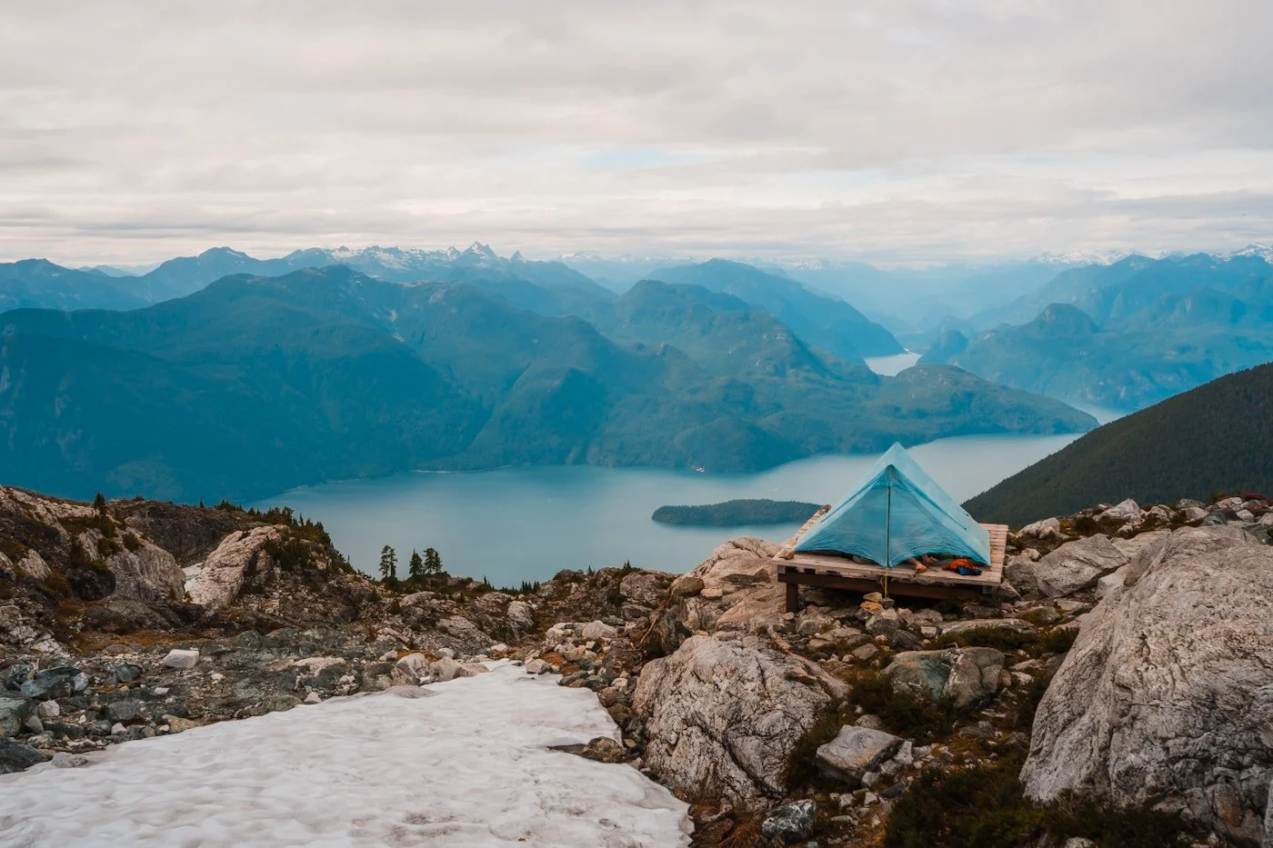 a blue tent on a tent platform on a rocky ridge overlooking a blue lake and coastal mountains at Panorama Ridge camping area in Golden Ears Provincial Park