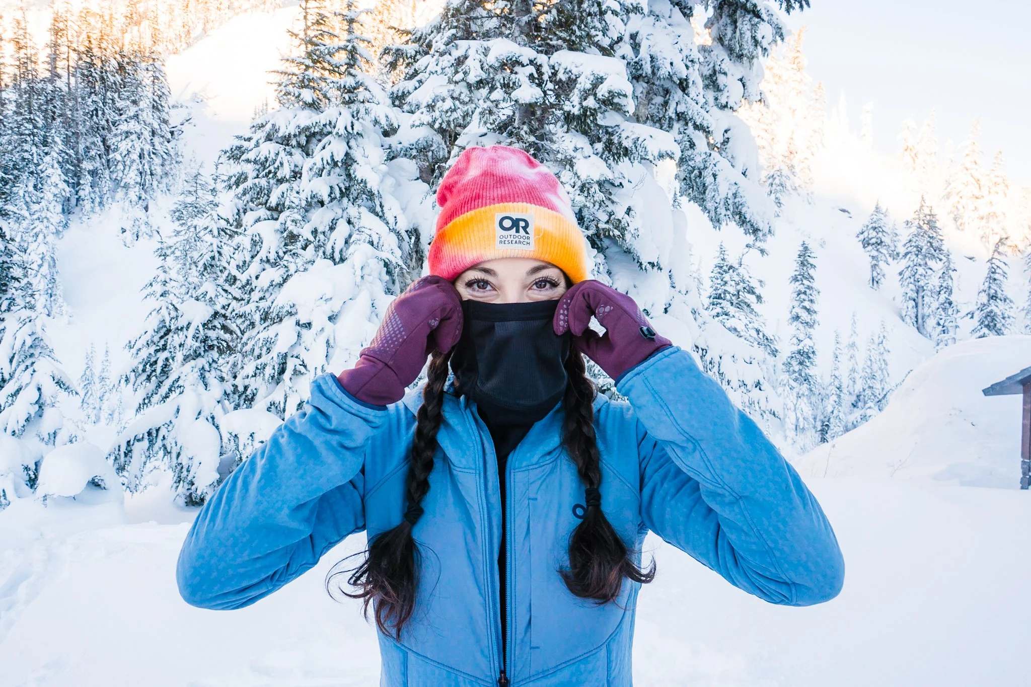 a women in the snow, wearing a colorful beanie, gloves and a buff