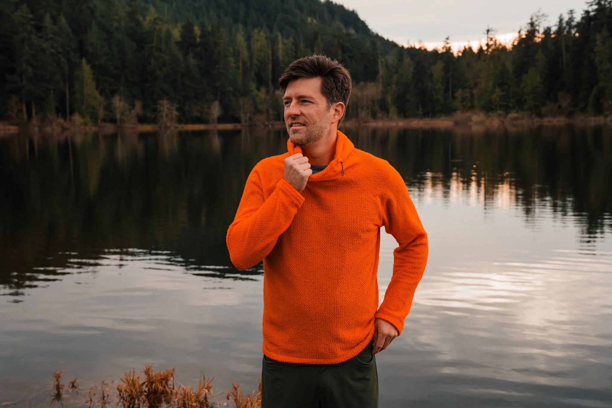 a man wearing a bright orange fleece hoodie, standing in front of a lake