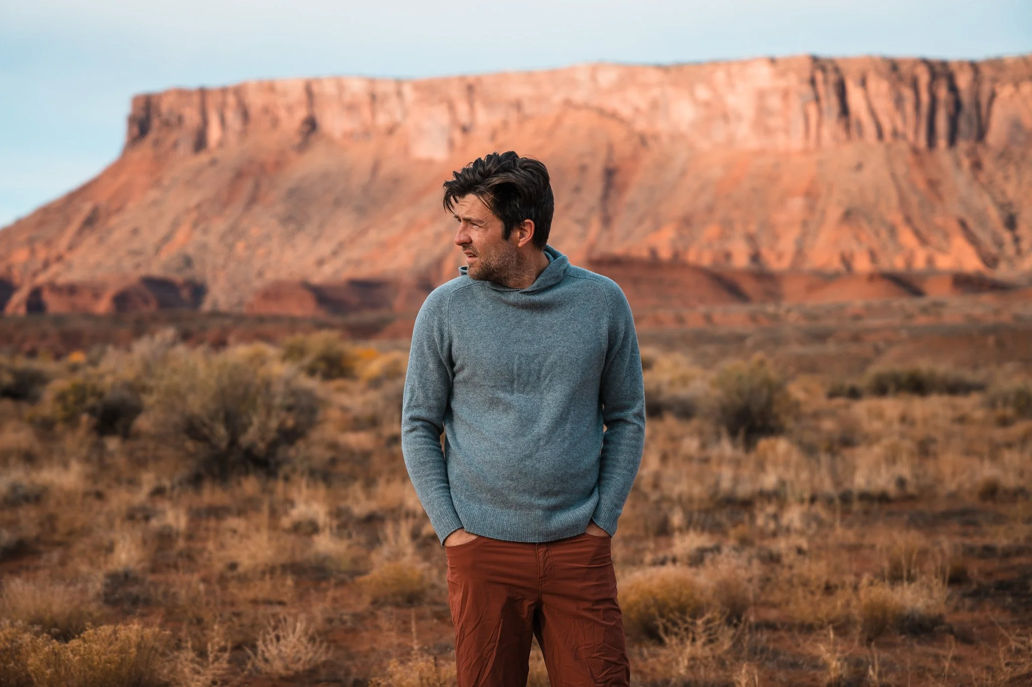 a man in a grey sweater and brown pants standing in the desert