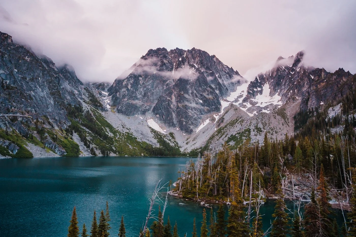 a bright blue colchuck lake with rocky peaks in the background and some clouds