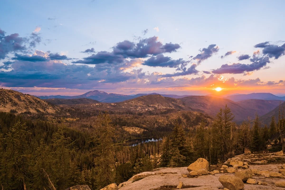 the sun setting over the cathedral lakes basin with hills and a lake below