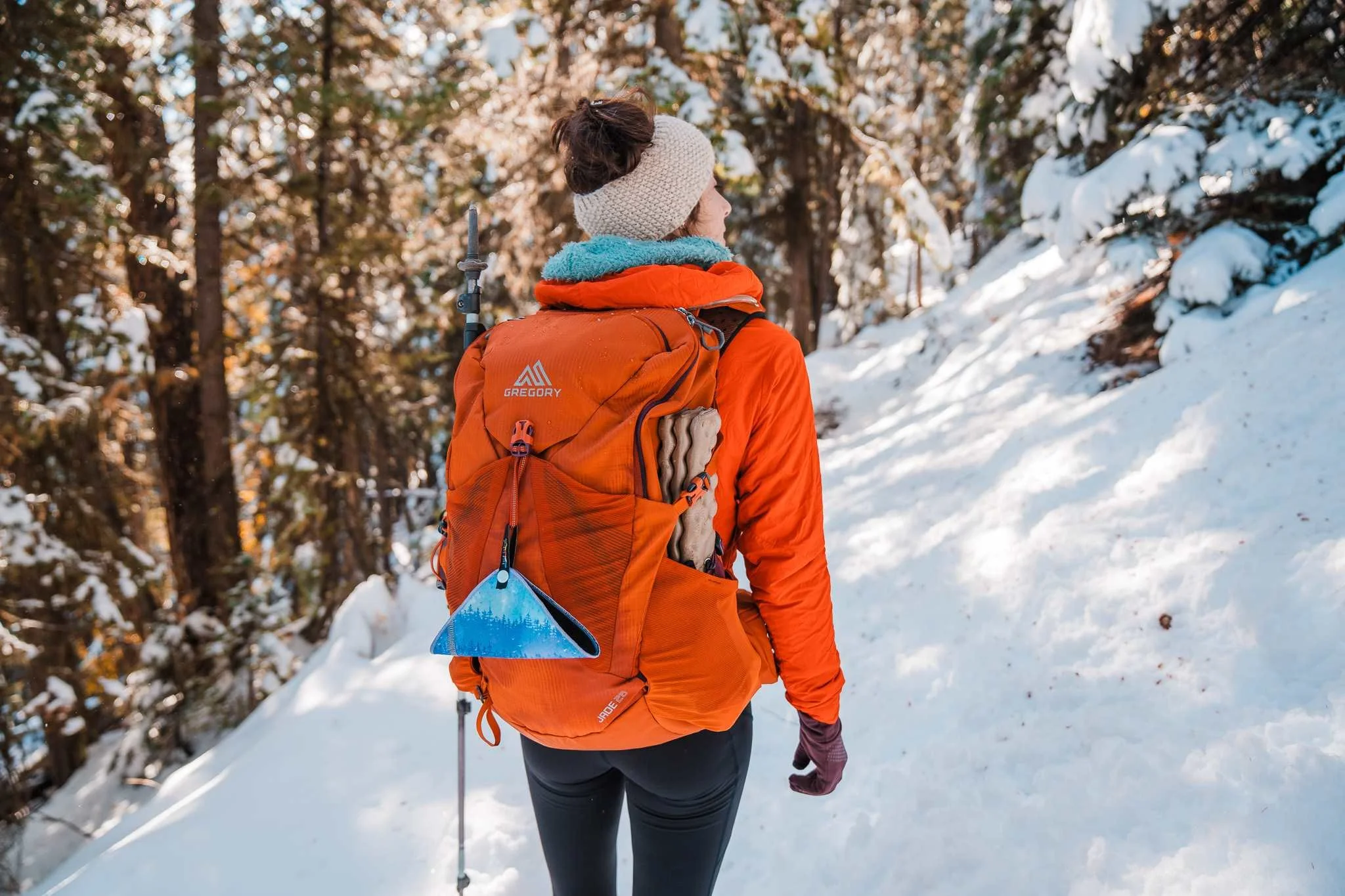 A women standing on a snowy hiking trail wearing a Gregory Jade 28L backpack while hiking