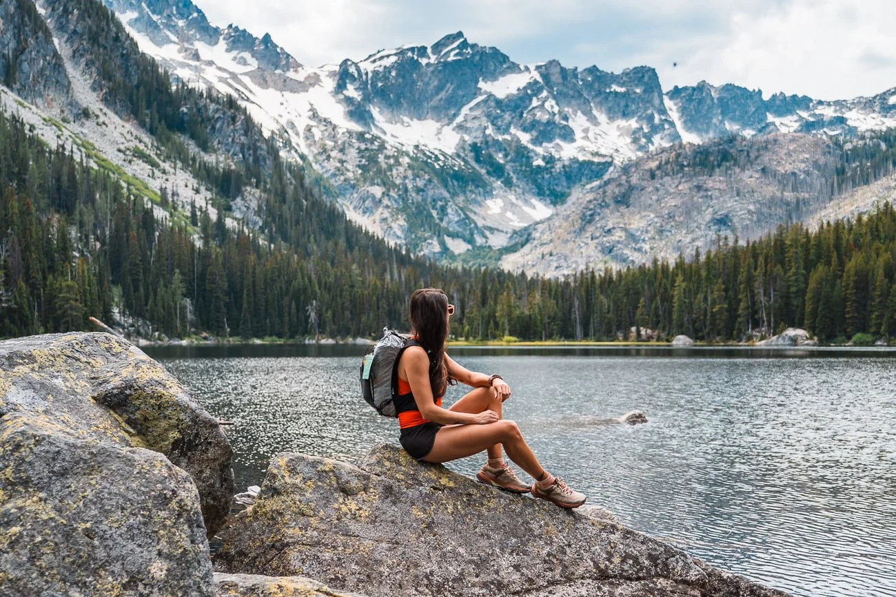 a hiker sitting on a rock in front of an alpine lake with mountains in the distance in the enchantments