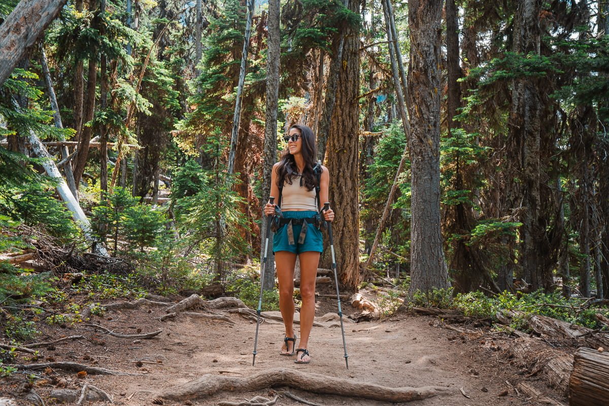 a woman hiking with trekking poles on a forested trail to colchuck lake