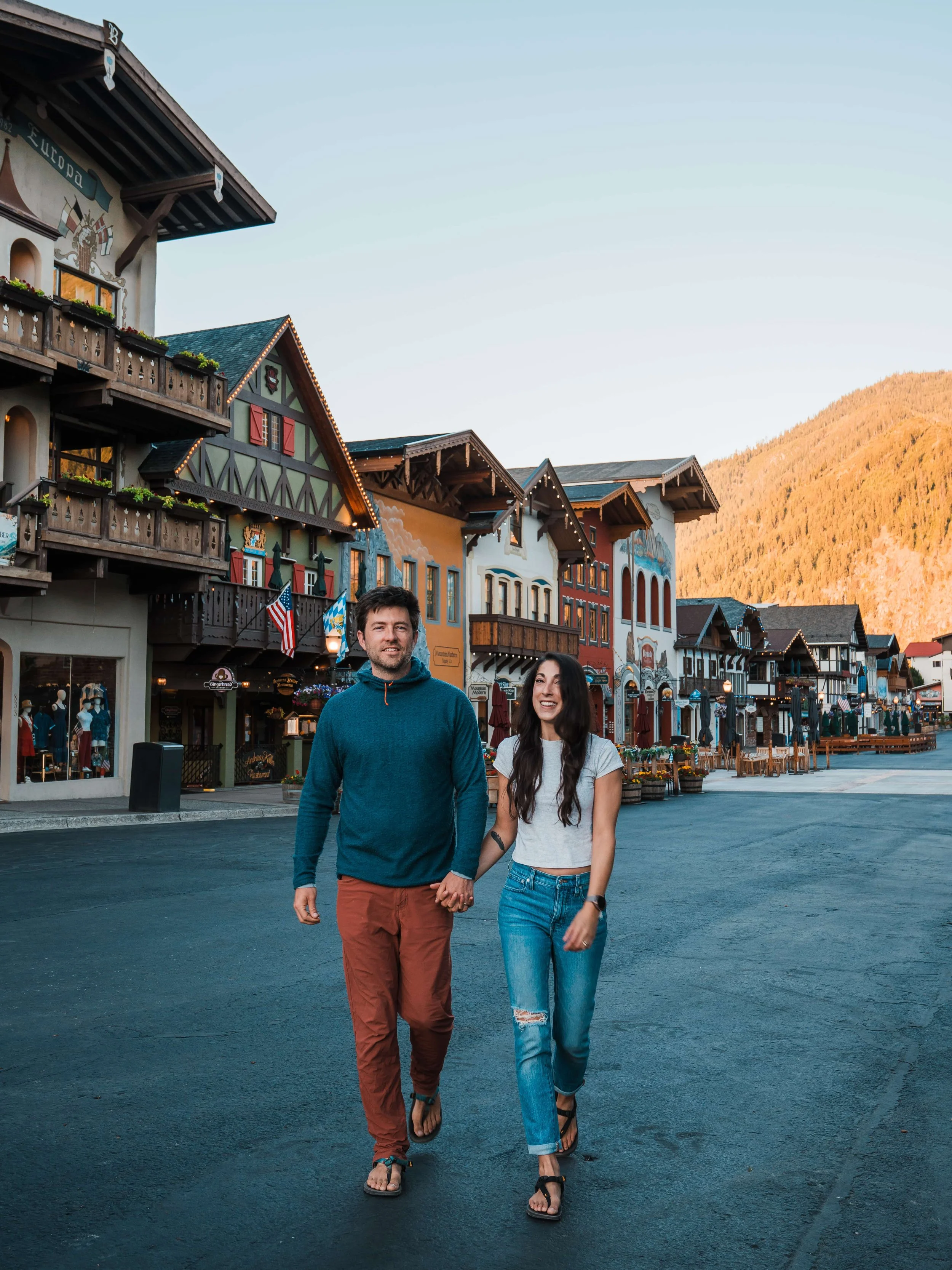 a couple holding hands, walking towards the camera with bavarian buildings in the background, in leavenworth, Washington