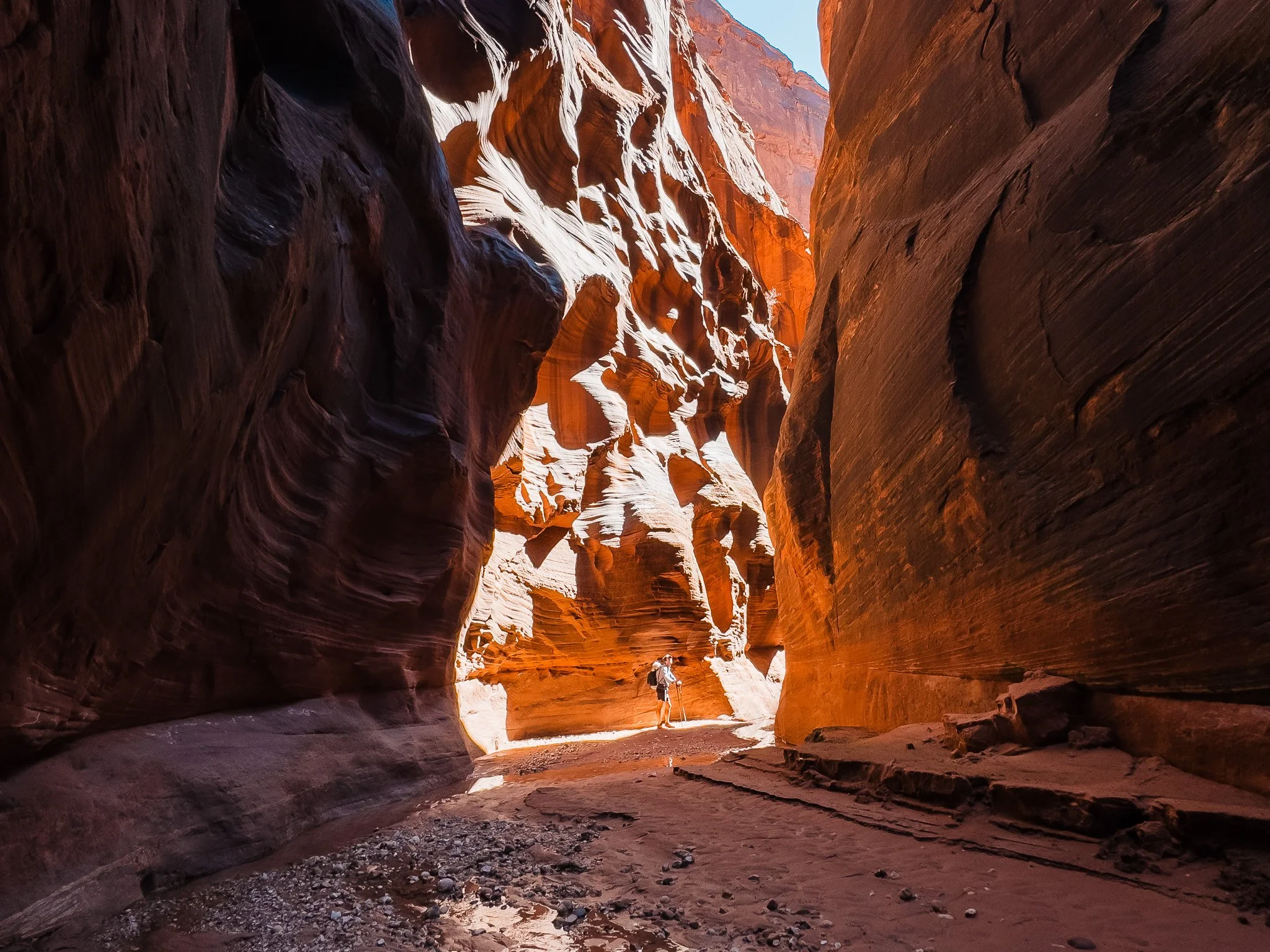 a tiny backpacker hiking deep in a slot canyon with light coming through and high red rock walls