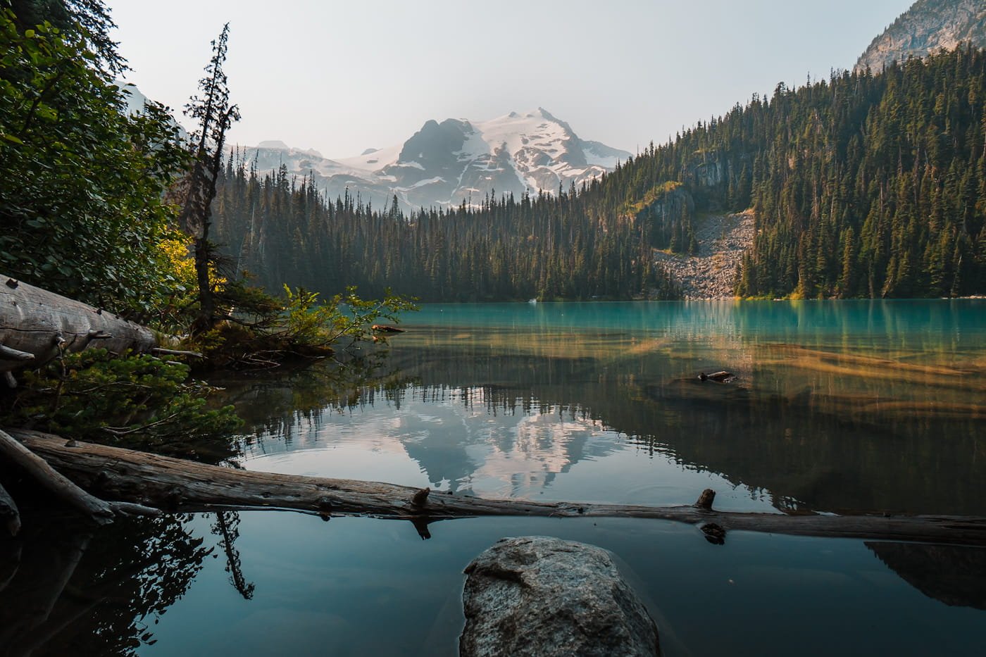 looking out at middle joffre lake, a bright blue lake with trees and a snowy mountain in the background