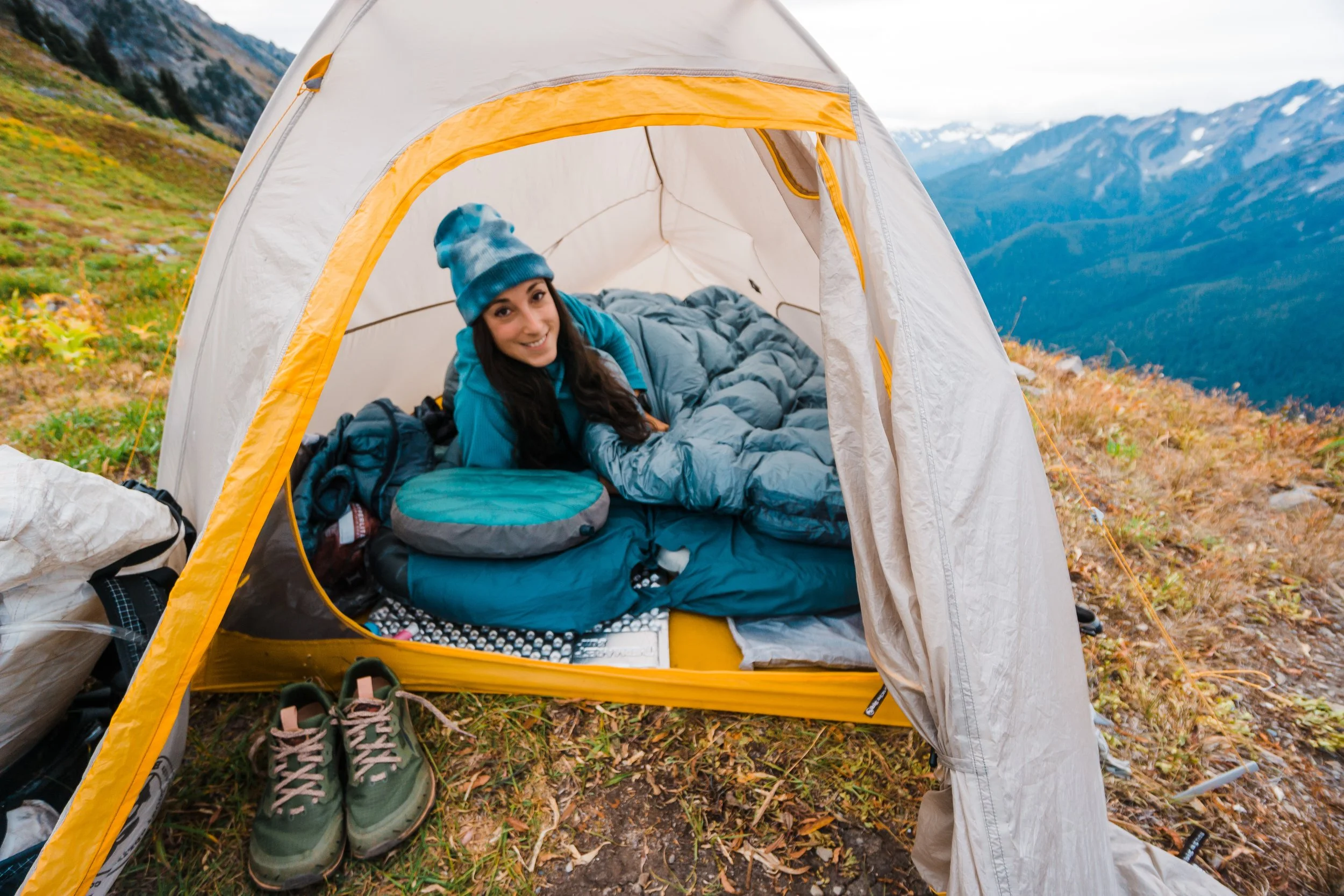 A woman lying in a tent on a mountain campground with scenic mountain views in the background.