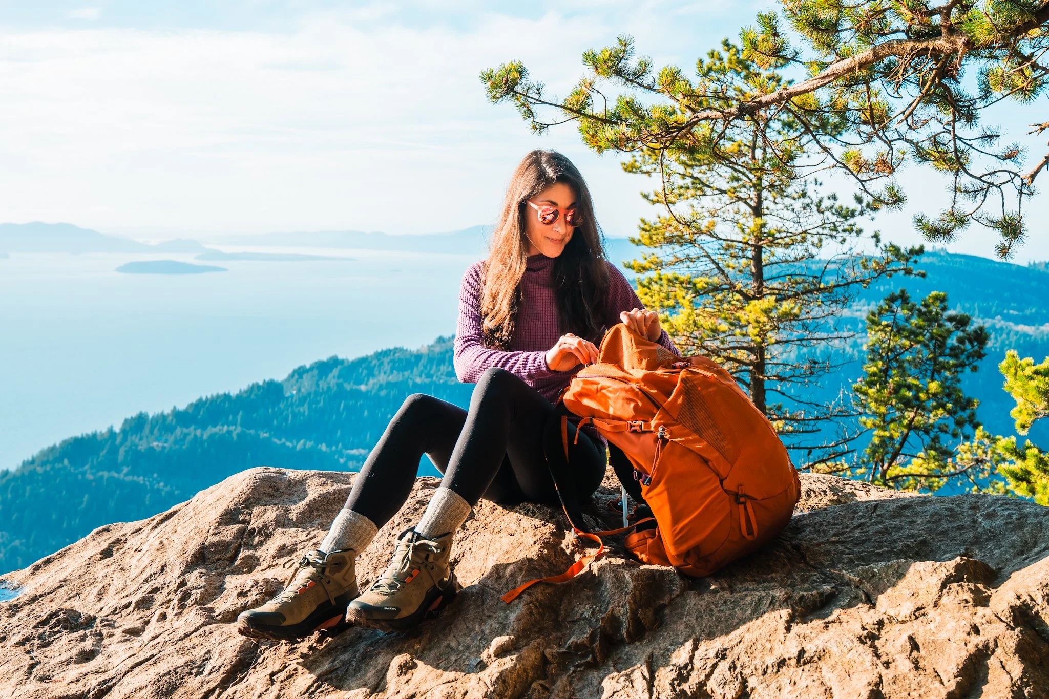 a woman sitting on a rock at a view point, pulling things out of her backpack