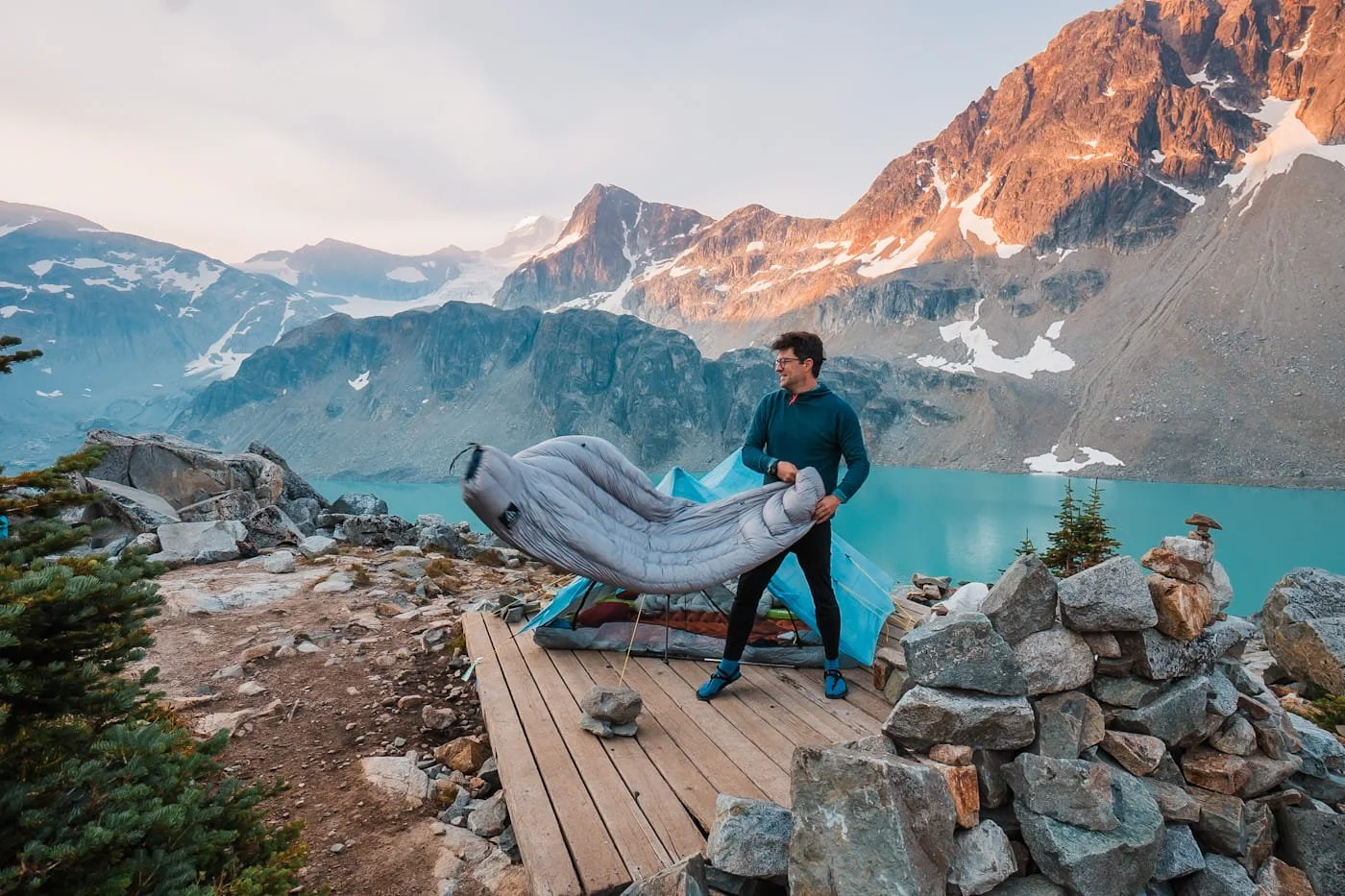 Backpacker standing with his camping quilt on a camping platform overlooking wedgemount lake