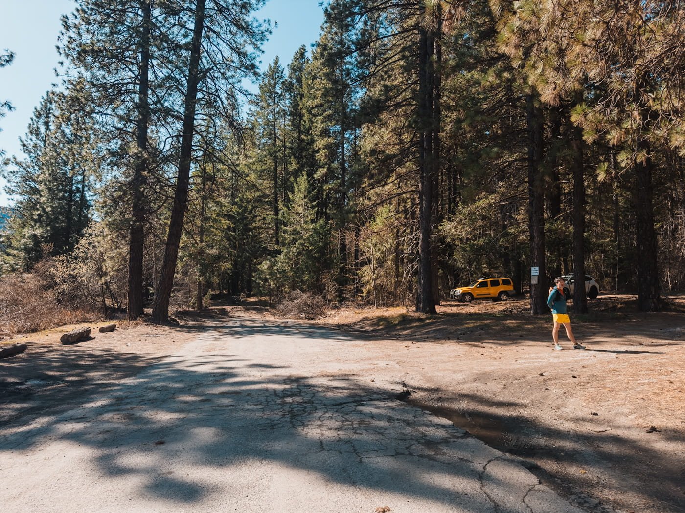 a dead end forest road, with a couple cars in the distance and a hiker, this is the parking for the icicle ridge trail
