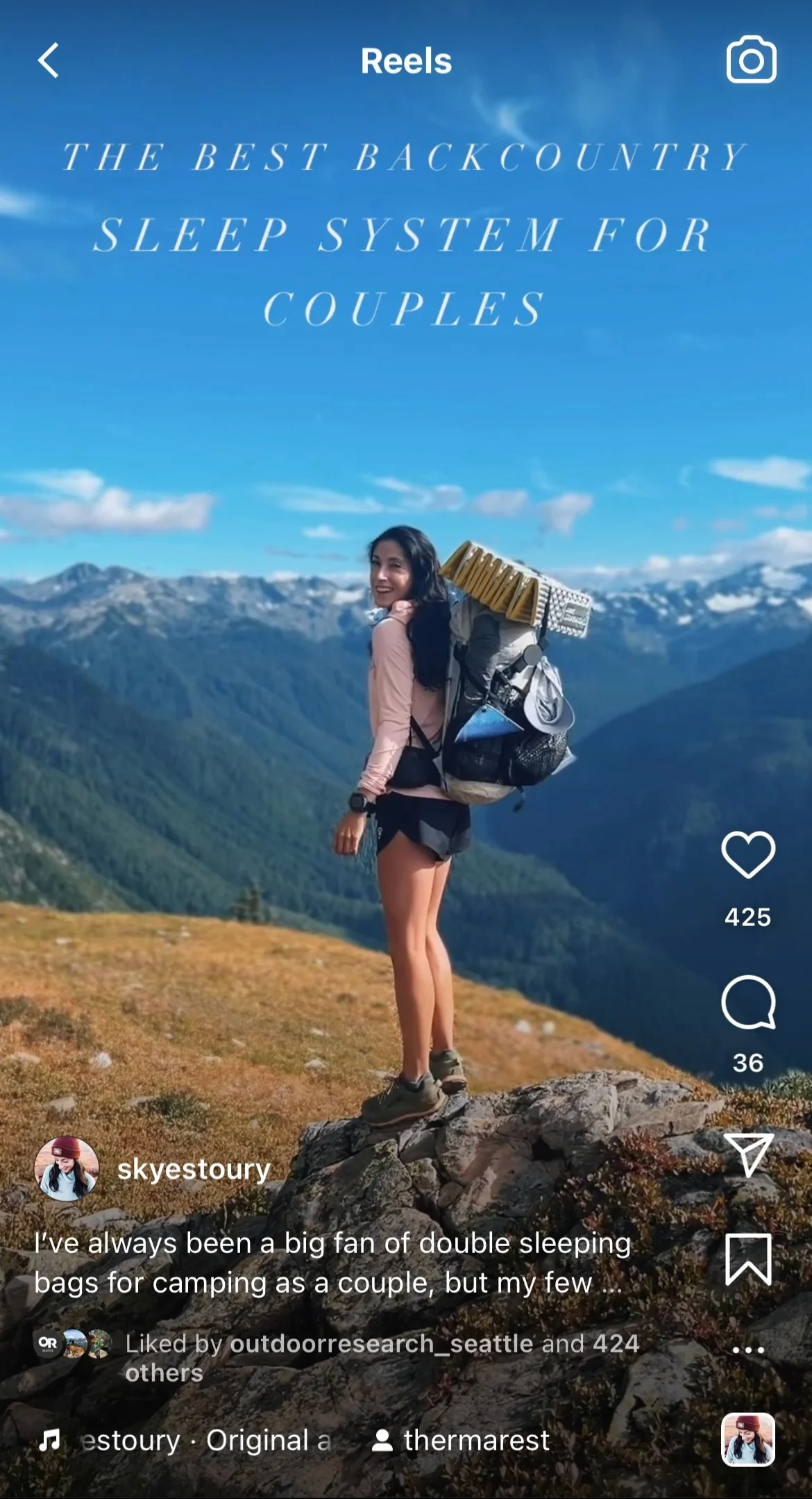 Woman with a large backpack and camping gear hiking on a mountain trail with mountains in the background and a blue sky.