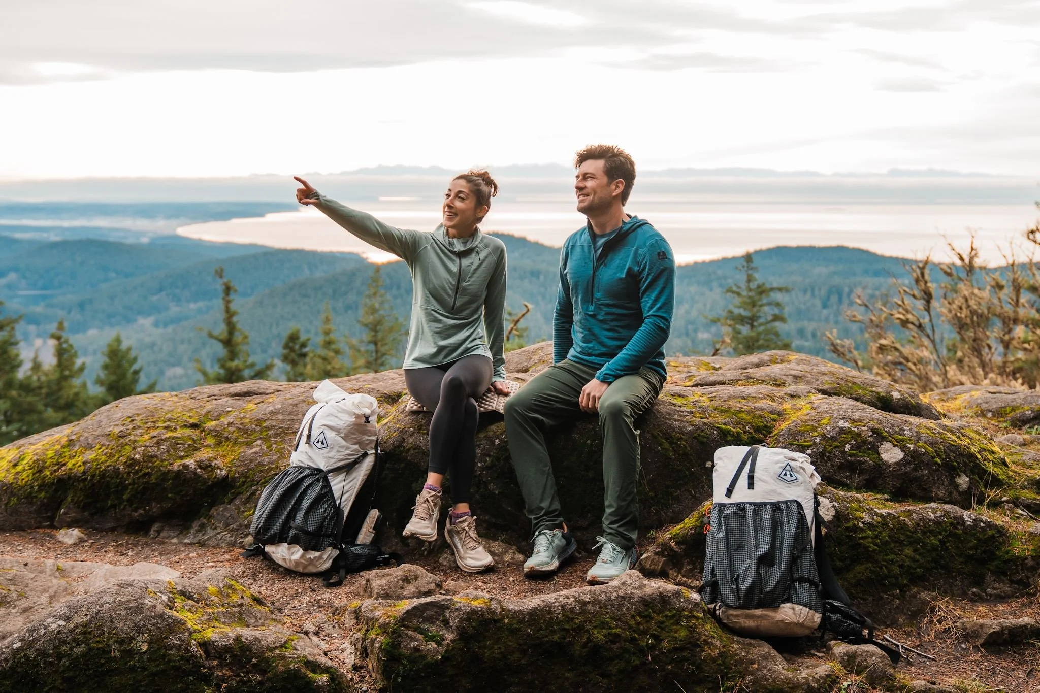 a couple sitting on rocks in front of a view of the sound, both wearing half zip fleece hoodies