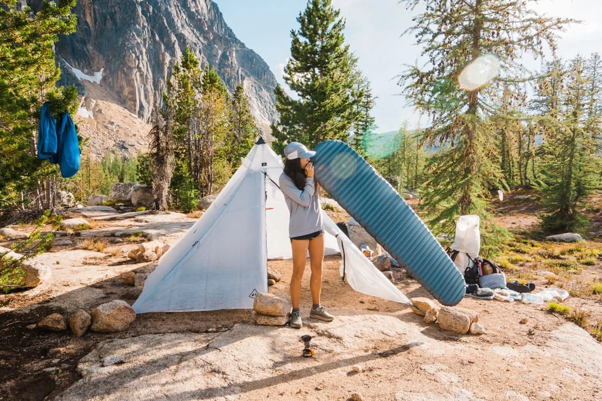 A woman blowing up a sleeping pad in front of a tent near Upper Cathedral Lake