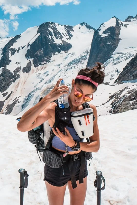 a woman wearing an ultralight backpacking pack with a white camera pod and water bottle pocket in the bugaboos with glaciated mountains in the background