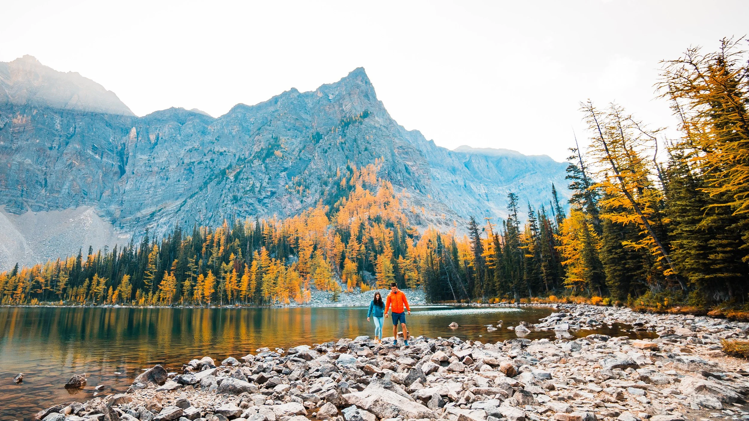 Couple walking along the shore of Arnica Lake during peak golden larch season