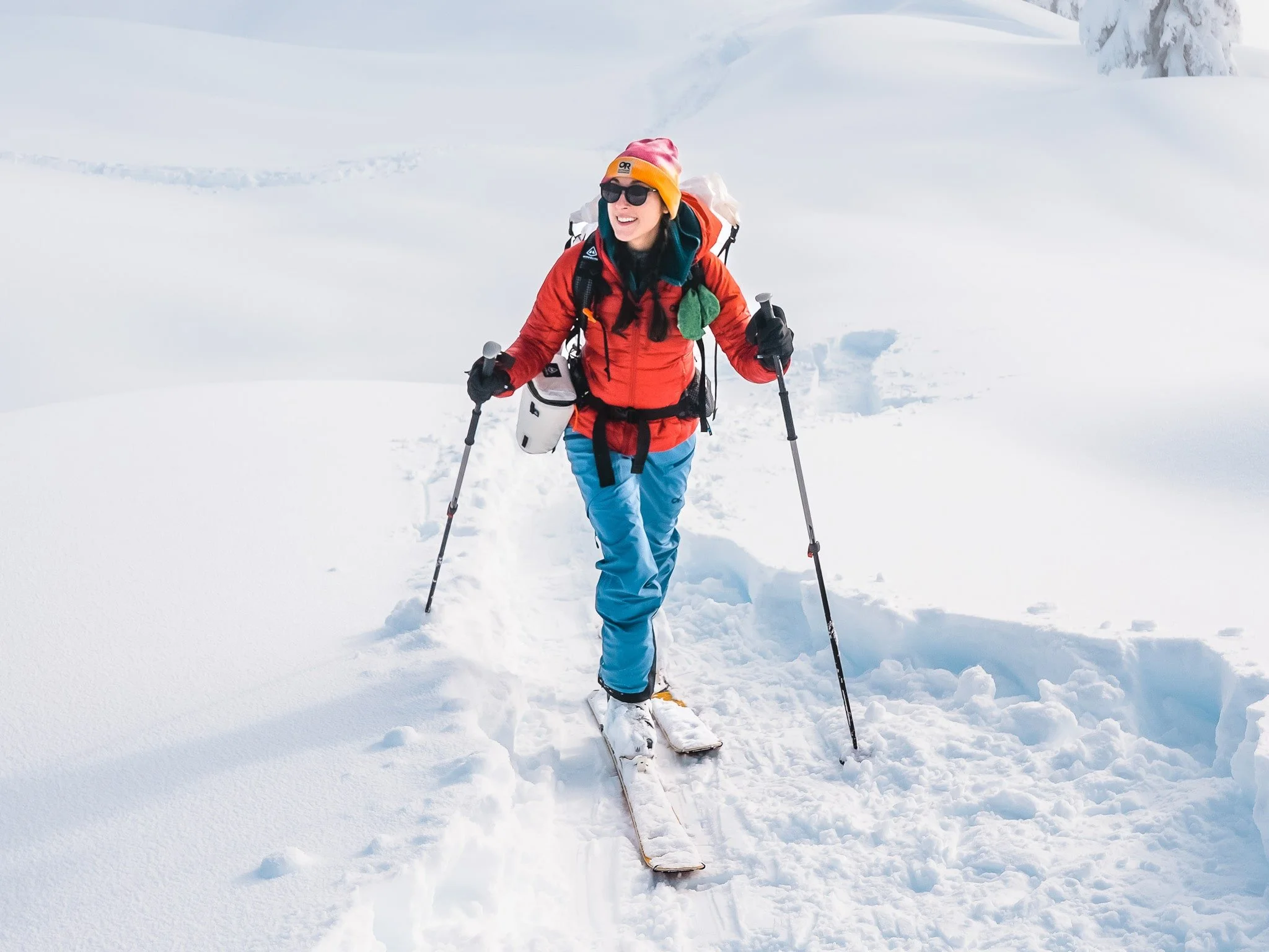 a woman ski touring on snow, wearing a bright red jacket and blue pants