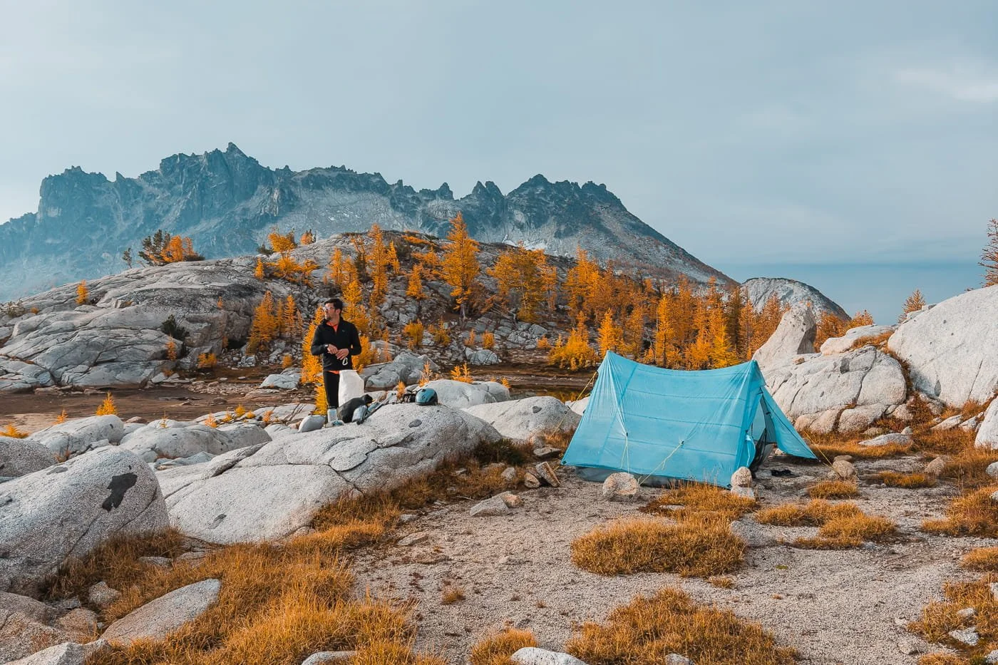 A blue zpacks trekking pole tent with a backpacker adding gear to his pack in the core enchantments