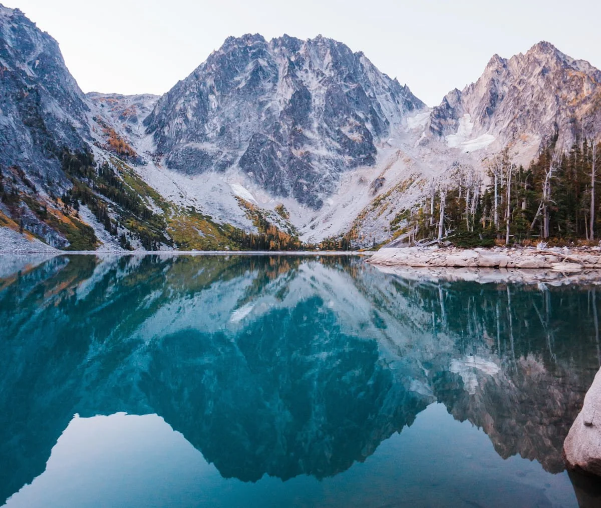 A reflective Colchuck lake, bright blue water with very rocky Dragontail peak and Colchuck peak in the background at blue hour