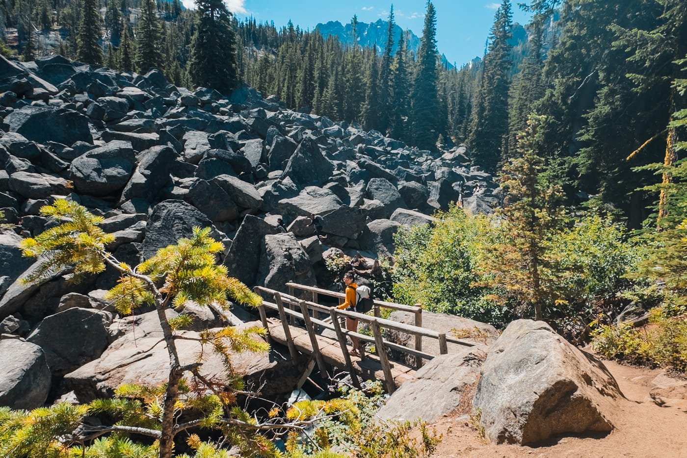 a backpacker hiking across a wooden bridge with a boulder field in the background