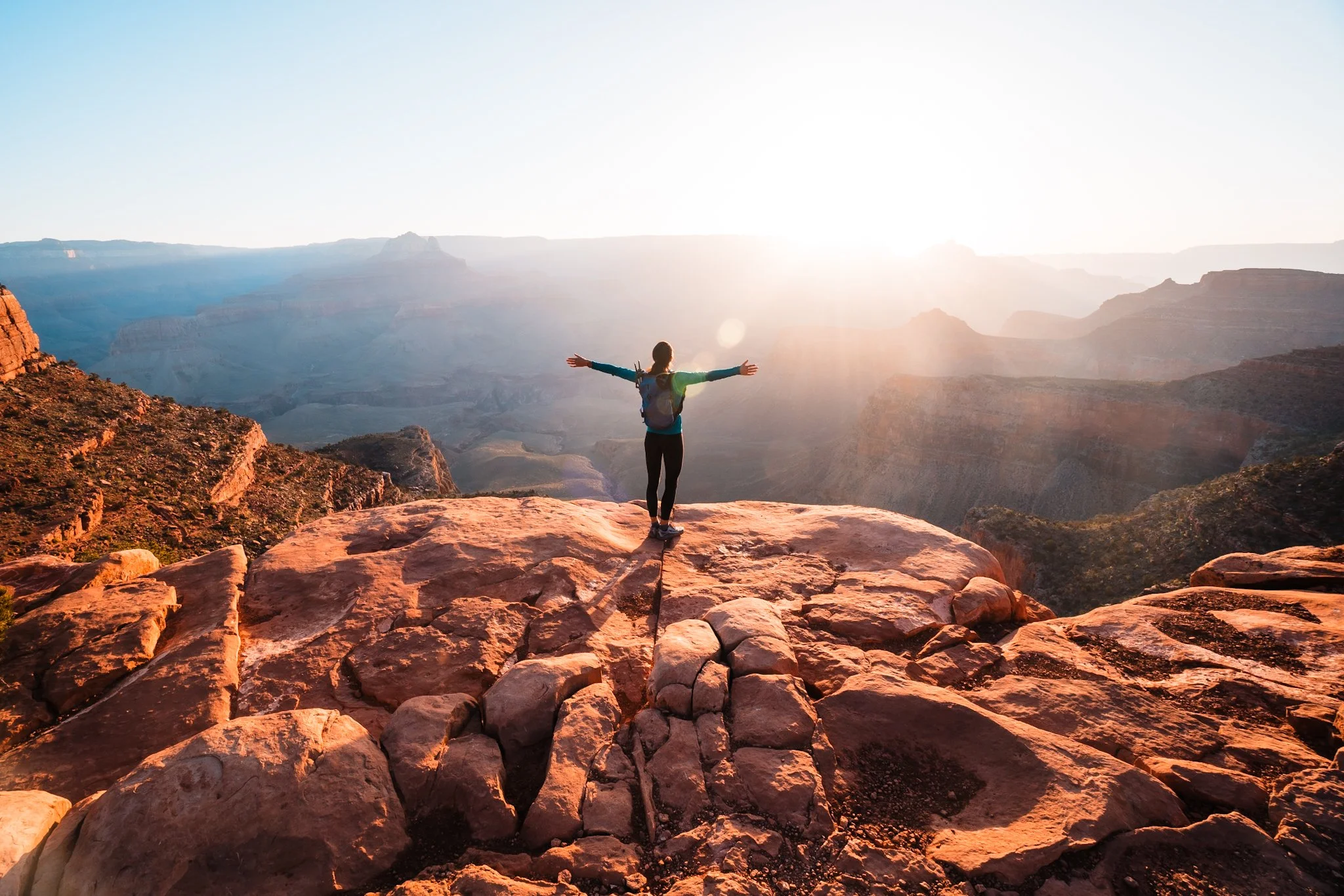 a women standing with her arms outstretched watching the sun rise in the grand canyon