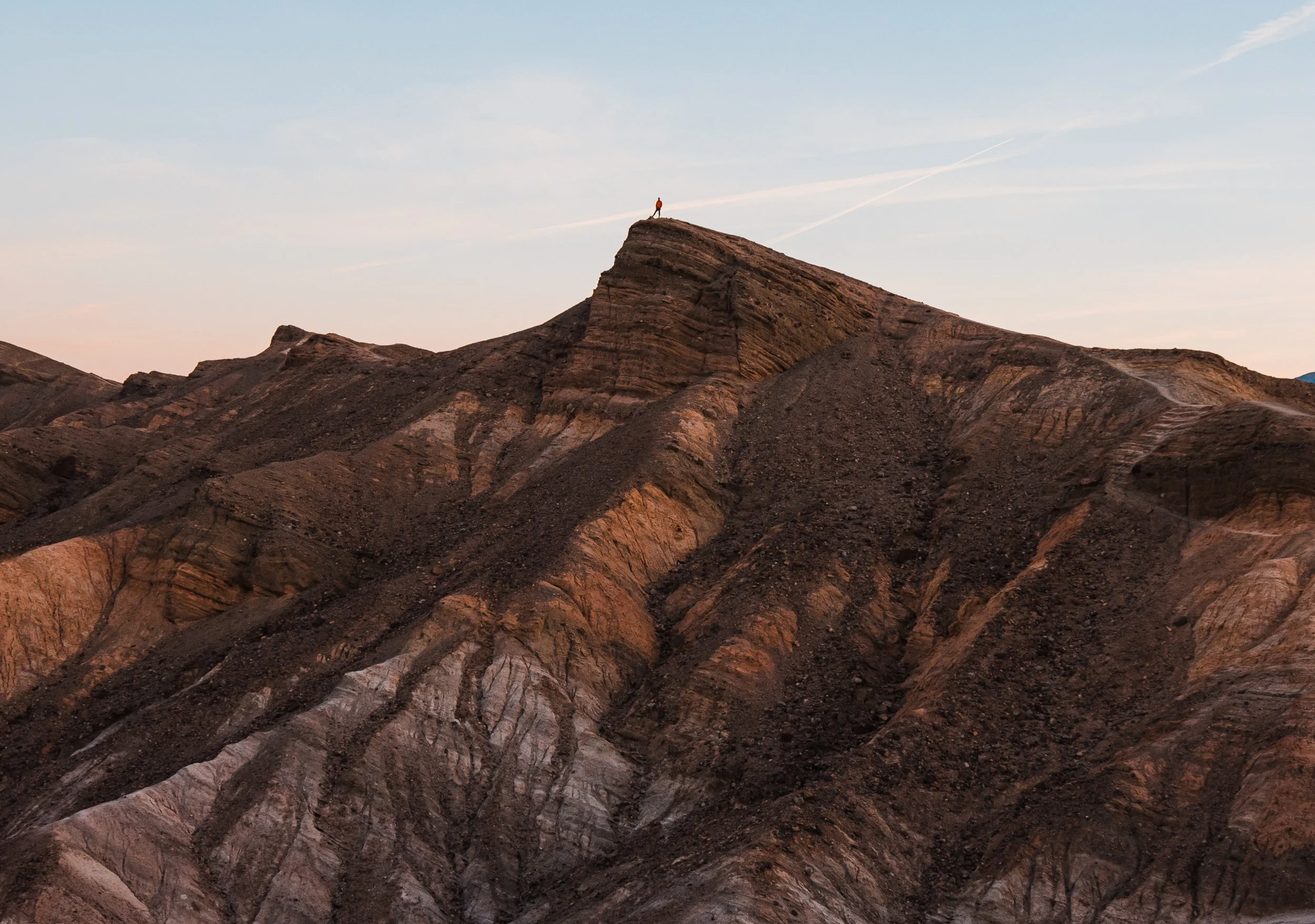 a tiny hiker standing on top of a mud hill in death valley national park