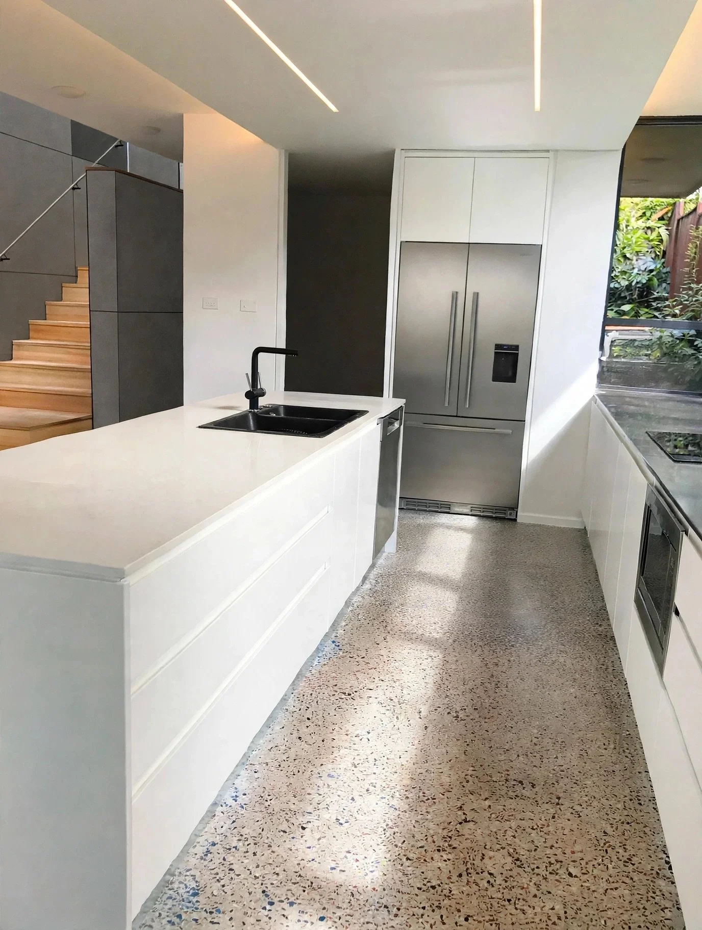Kitchen island with polished concrete flooring, integrated black sink and full-height stainless steel refrigeration, Marrickville renovation
