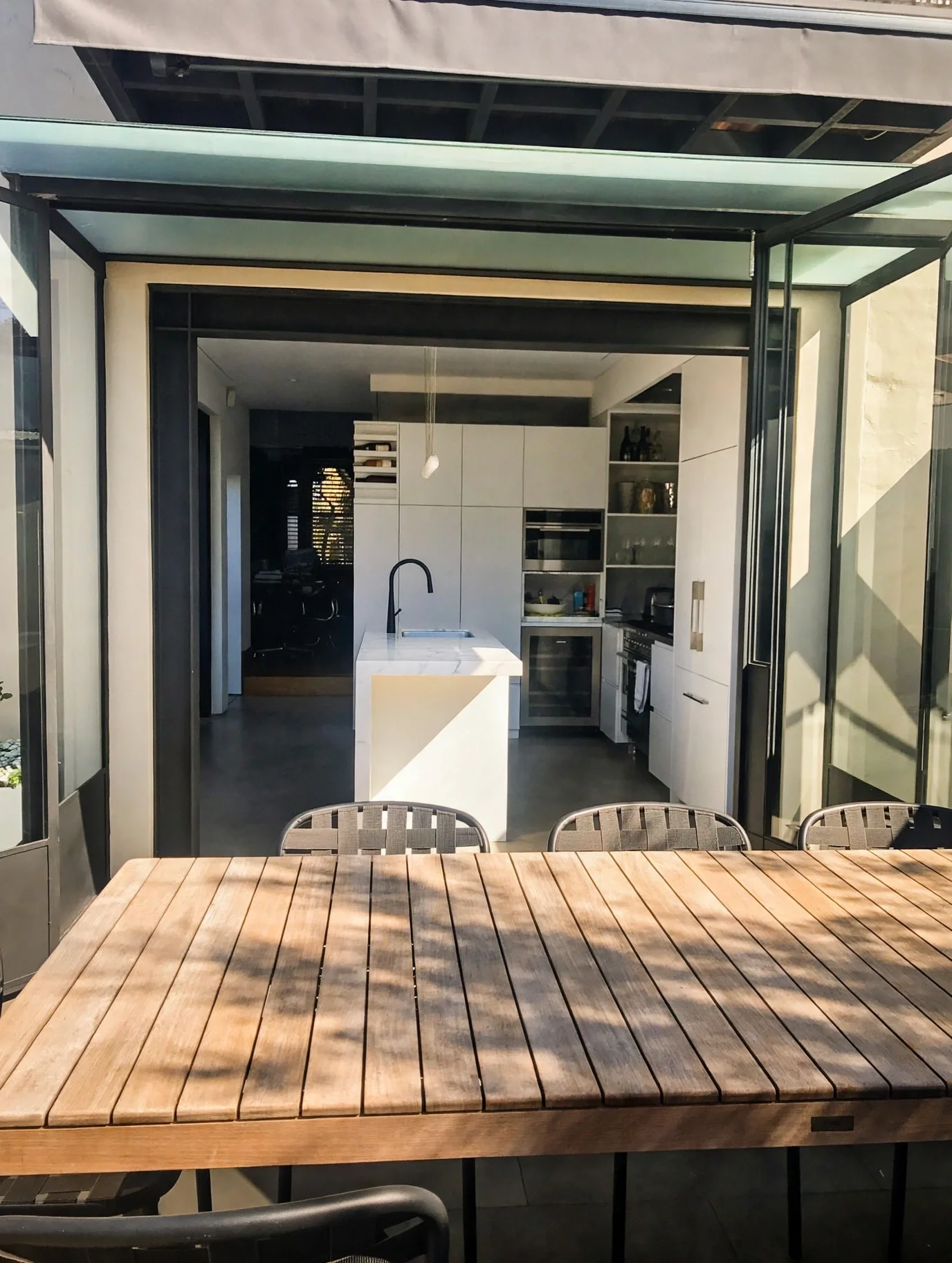Kitchen and dining area extending onto timber deck through steel-framed glazing, Erskineville terrace