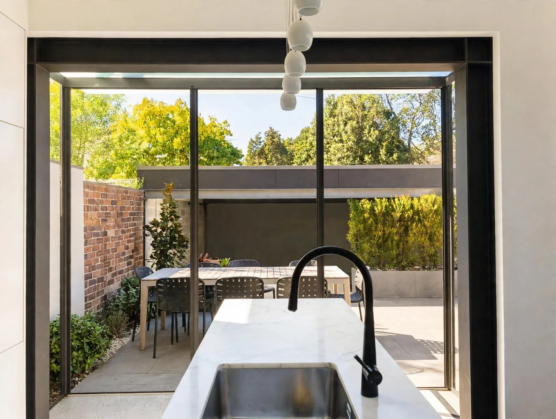 Kitchen island framed by full-height steel glazing, opening to courtyard dining area, Erskineville terrace renovation