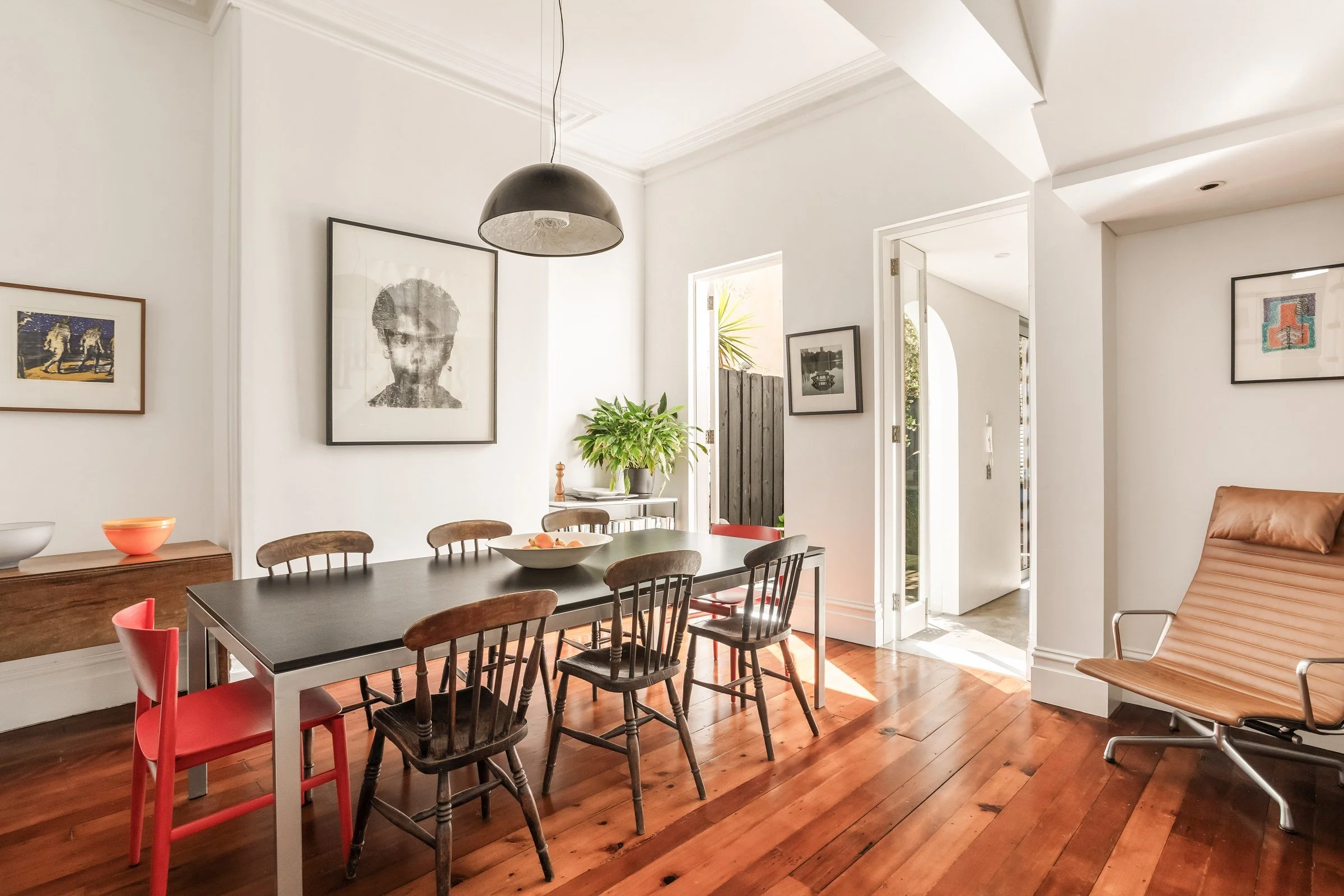 Dining room in a Surry Hills terrace with a black table, timber chairs, a red chair and polished timber floors, by A Studio Architecture