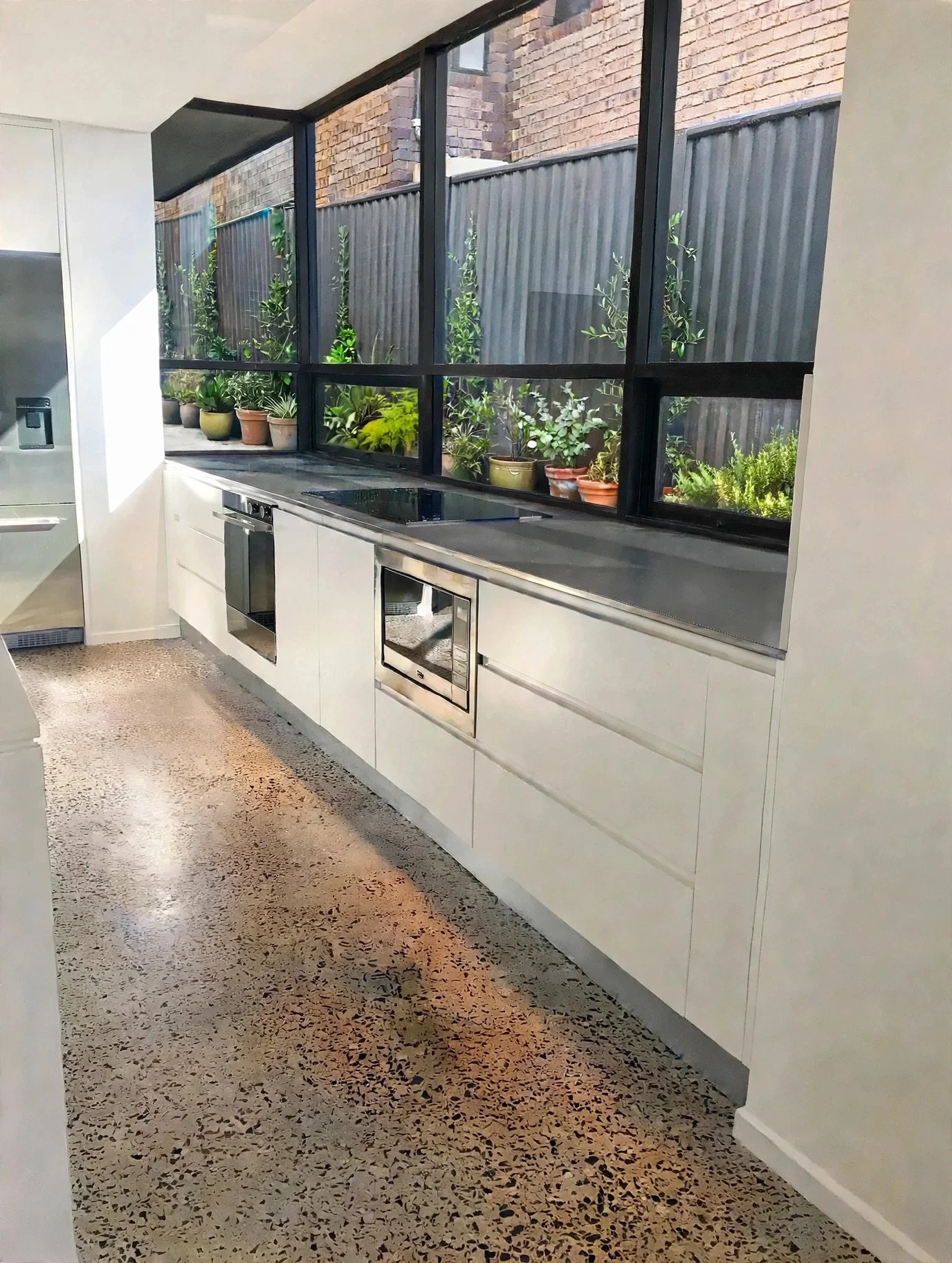 Kitchen cooking wall with stainless steel benchtop, integrated appliances and steel-framed window, Marrickville renovation