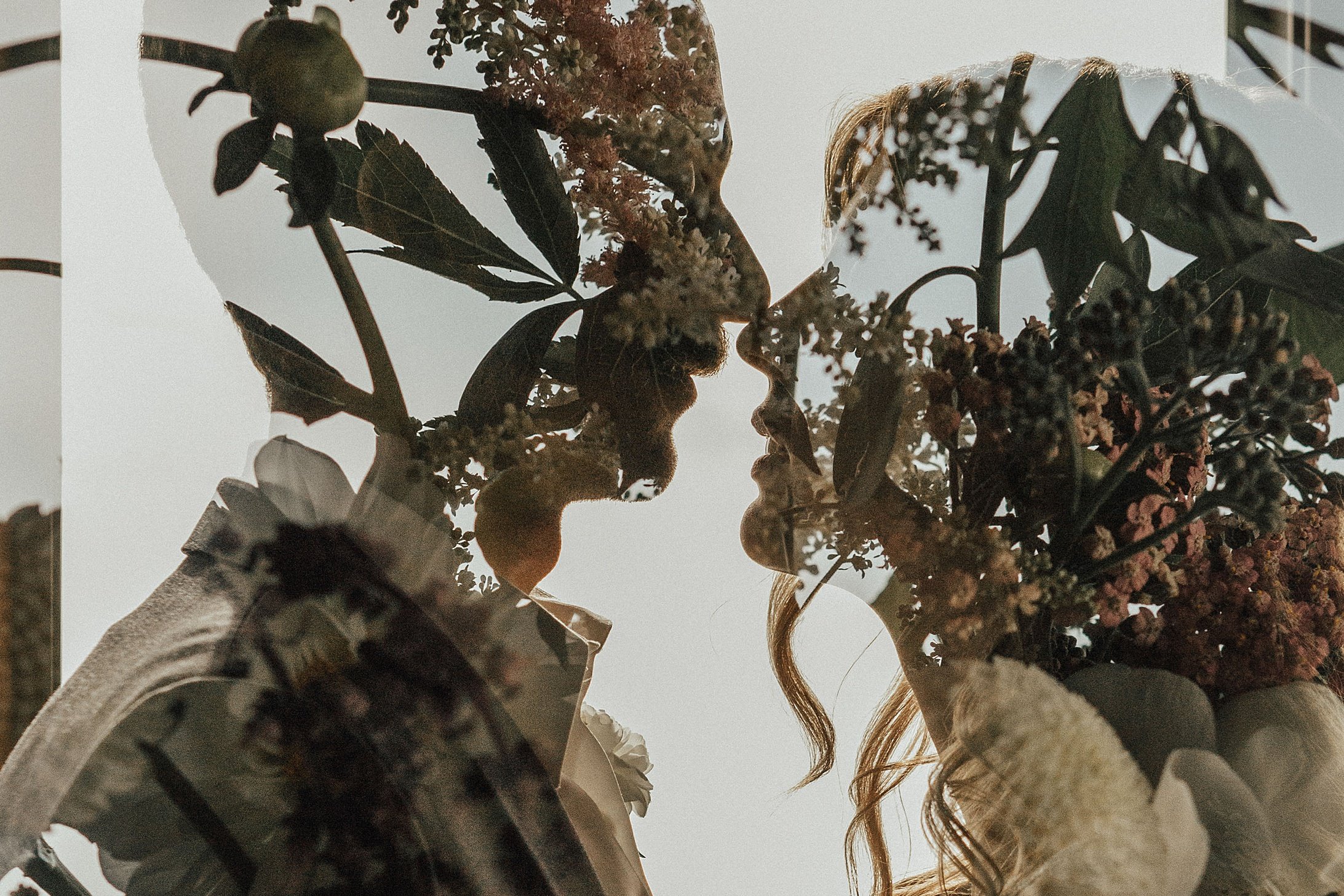 Two women facing each other, holding bouquets of flowers, with their profiles seen against a bright sky.