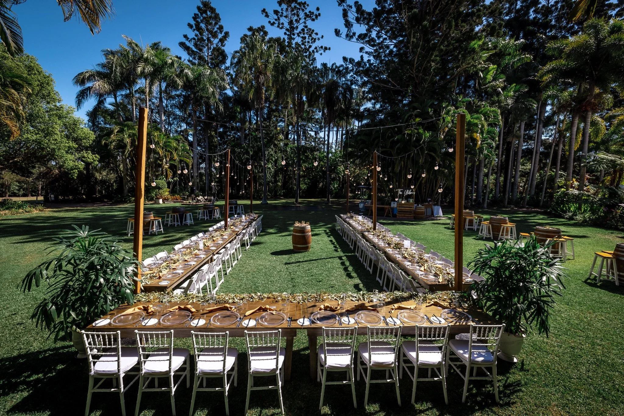 Long banquet-style reception table set outdoors for a garden wedding with natural greenery surrounds.
