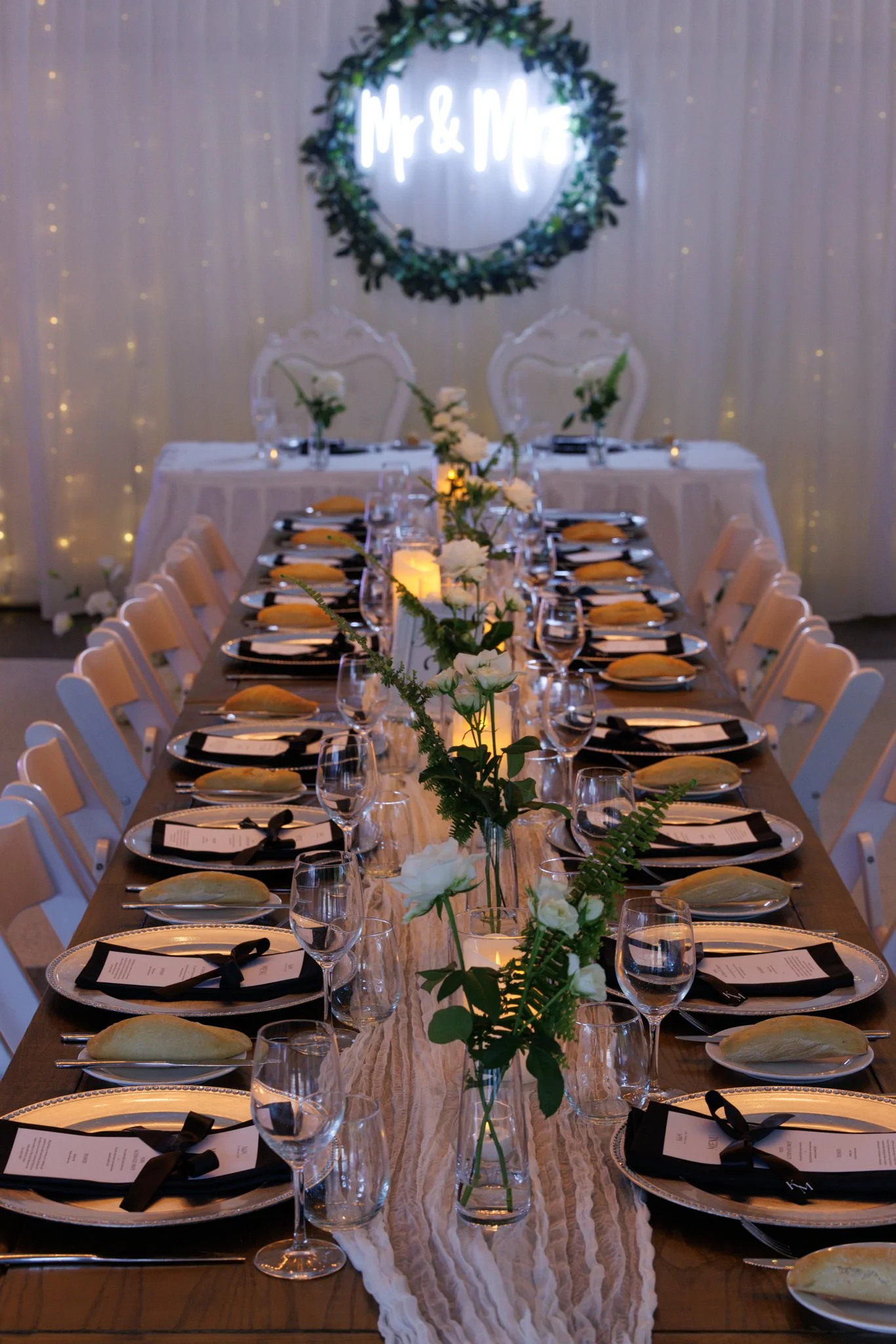 Long reception table styled with greenery runners, candles and coordinated tableware for a modern wedding look.
