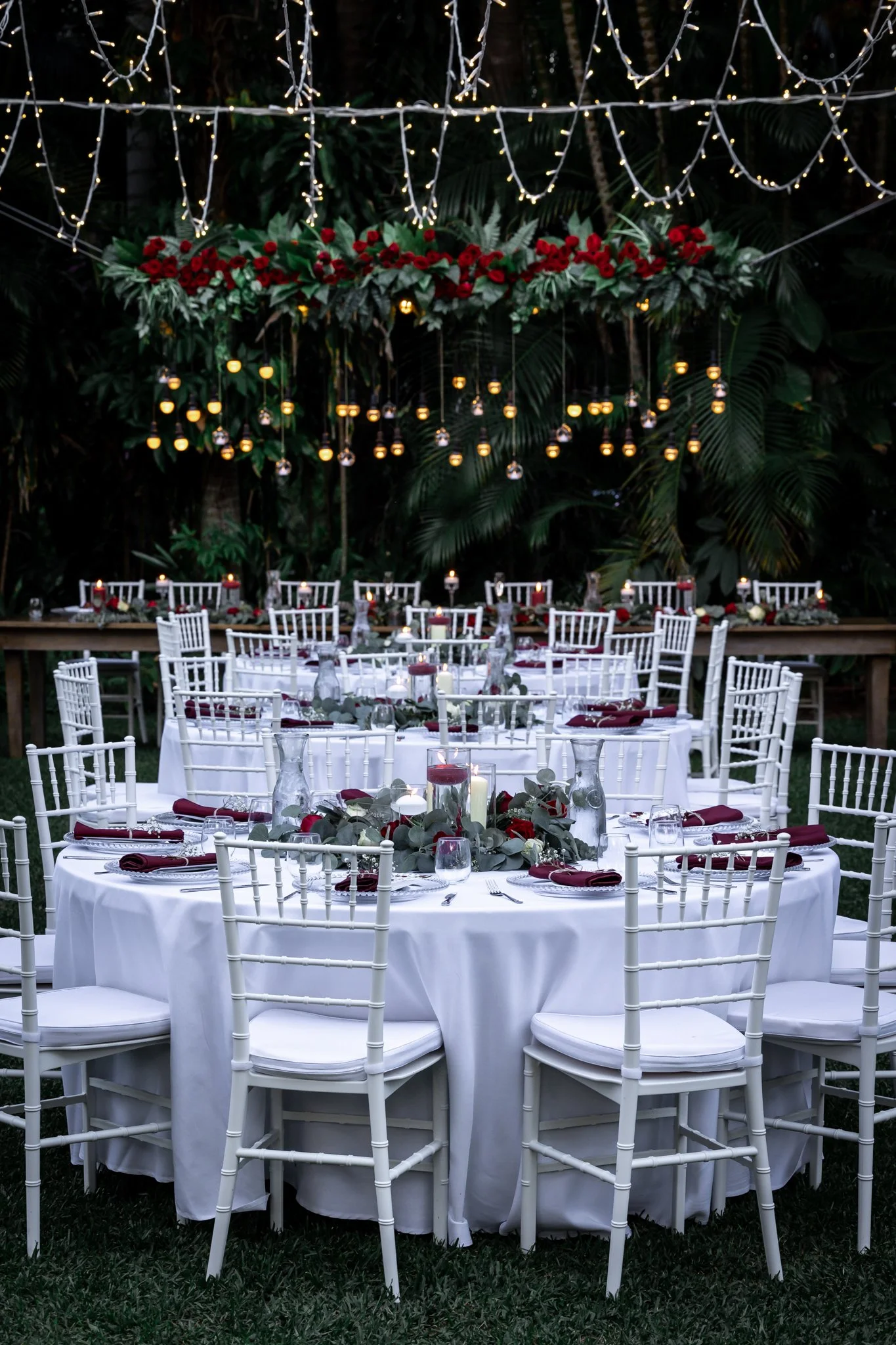 Beautifully styled round reception tables with white linens and floral centrepieces in a garden setting.