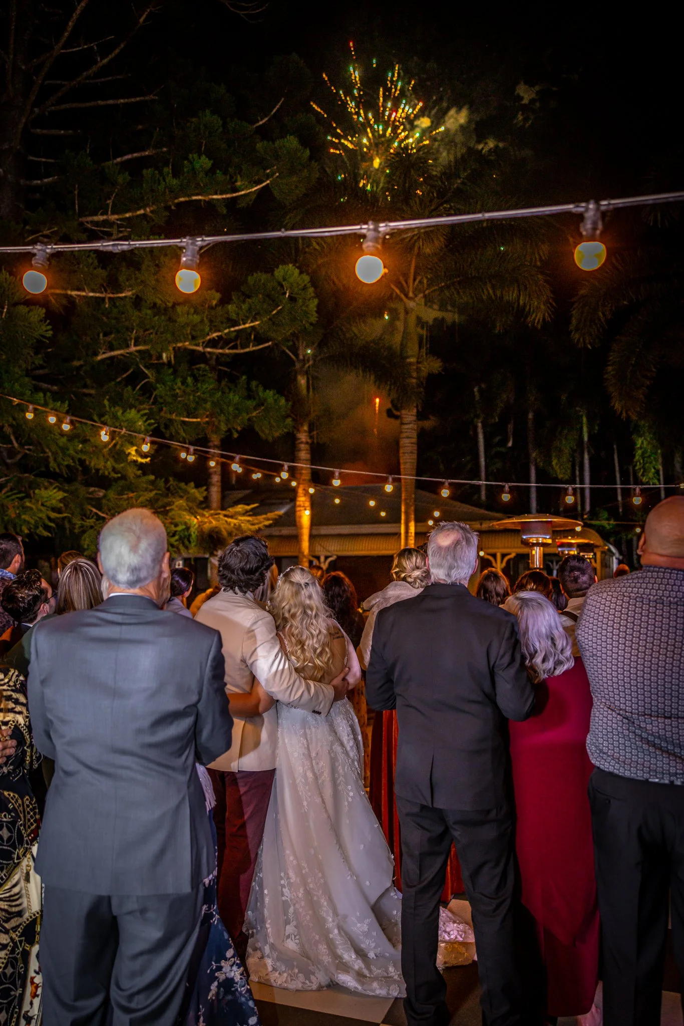 Wedding fireworks lighting up the night sky above a garden reception celebration.