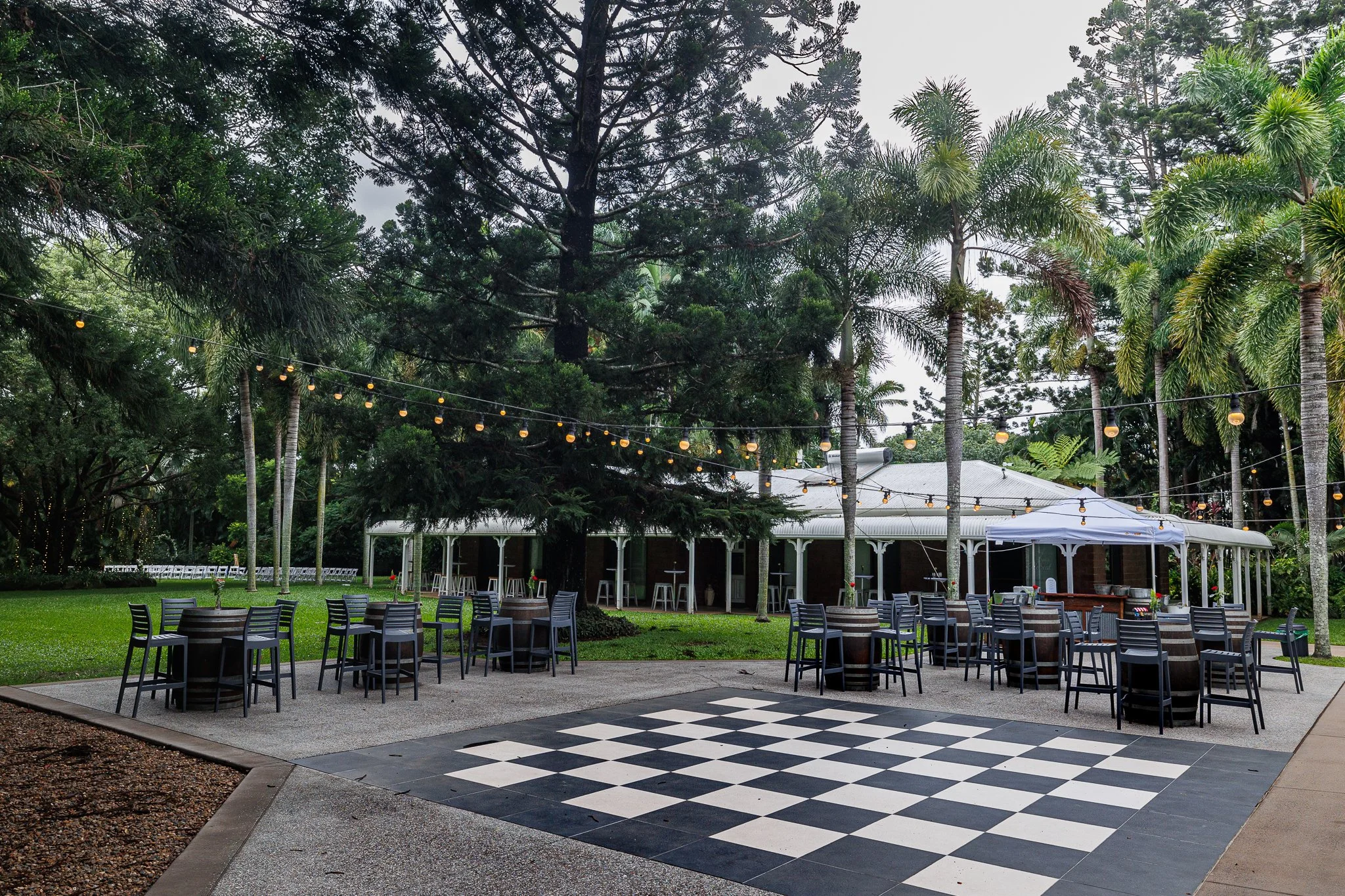 Patio with barrel tables, chairs and a chequered dance floor beside the house verandahs and gardens at In The Grove.