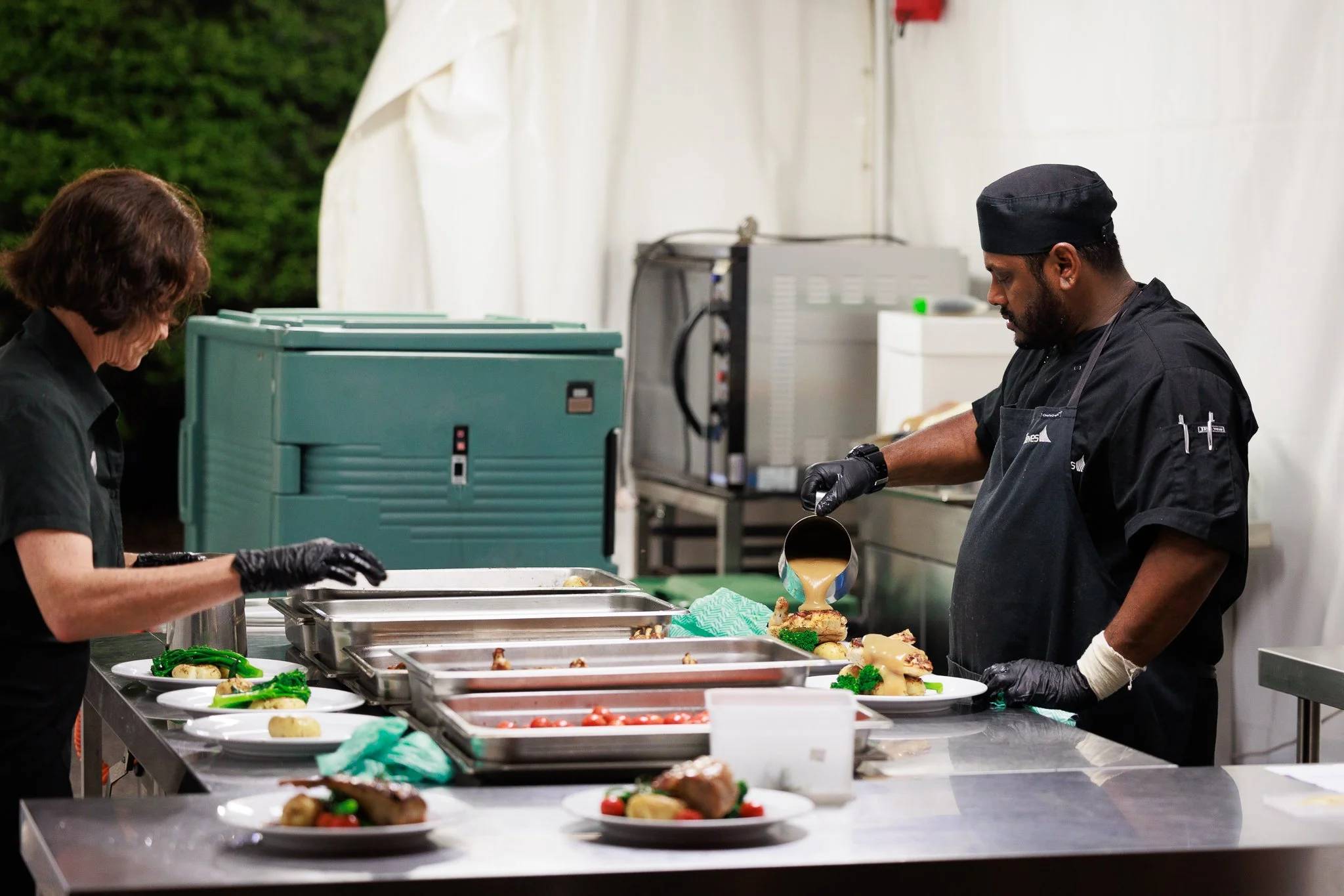 Professional wedding catering team preparing and plating meals for guests behind the scenes.