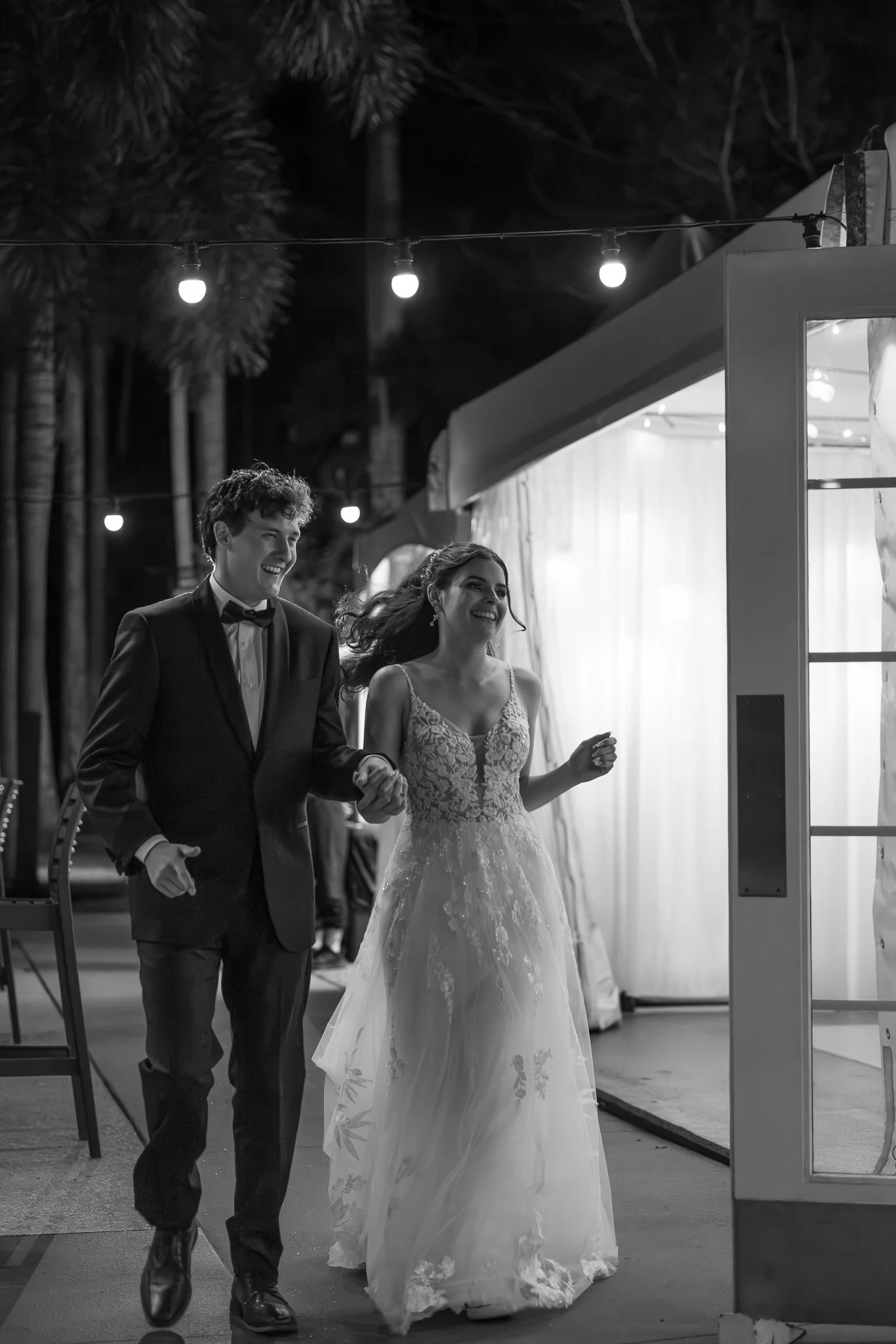 Newlyweds entering their reception marquee at night under glowing festoon lighting.