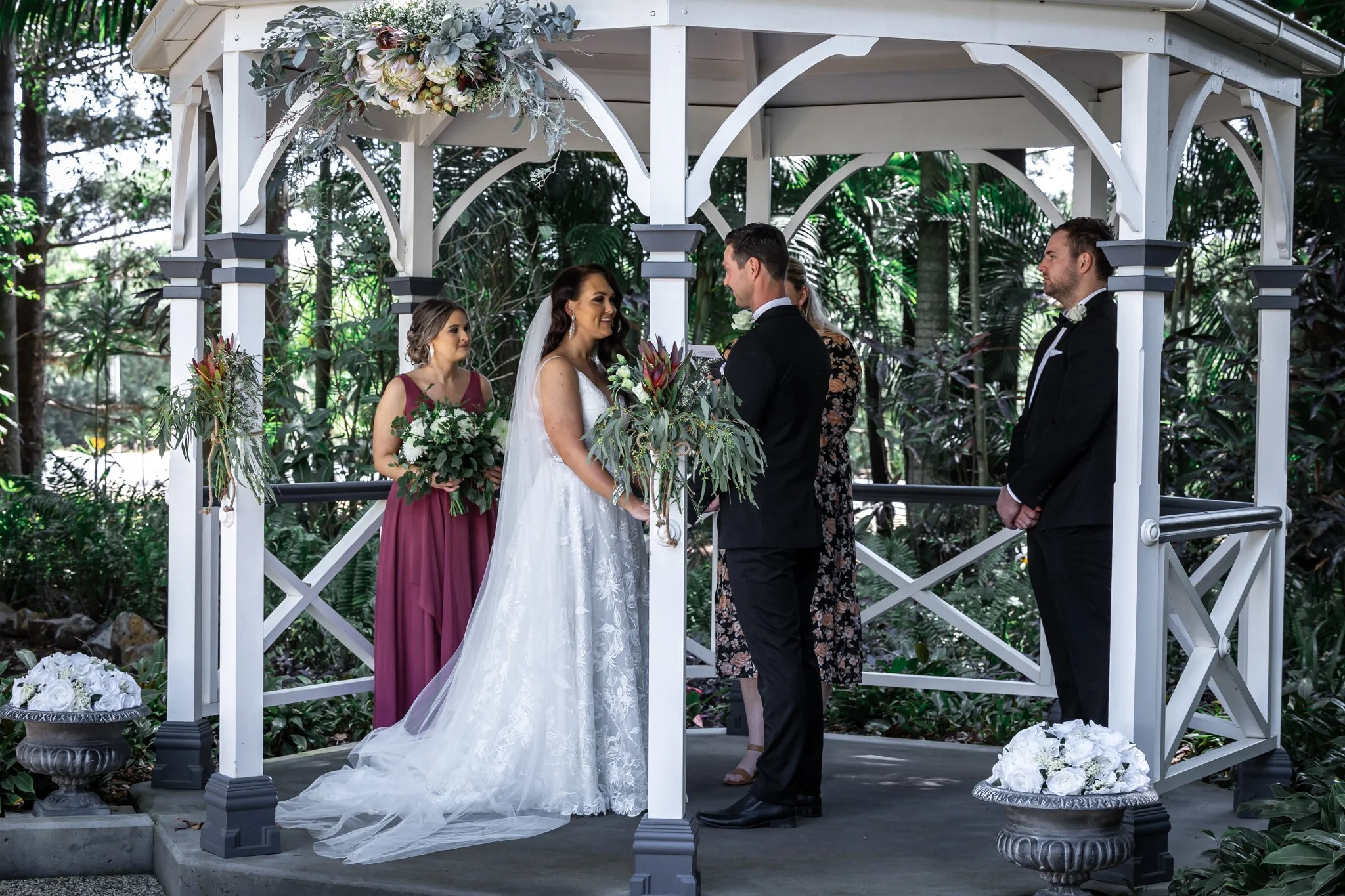 Bride and groom exchanging vows in a romantic gazebo ceremony surrounded by lush gardens at a Queensland wedding venue.