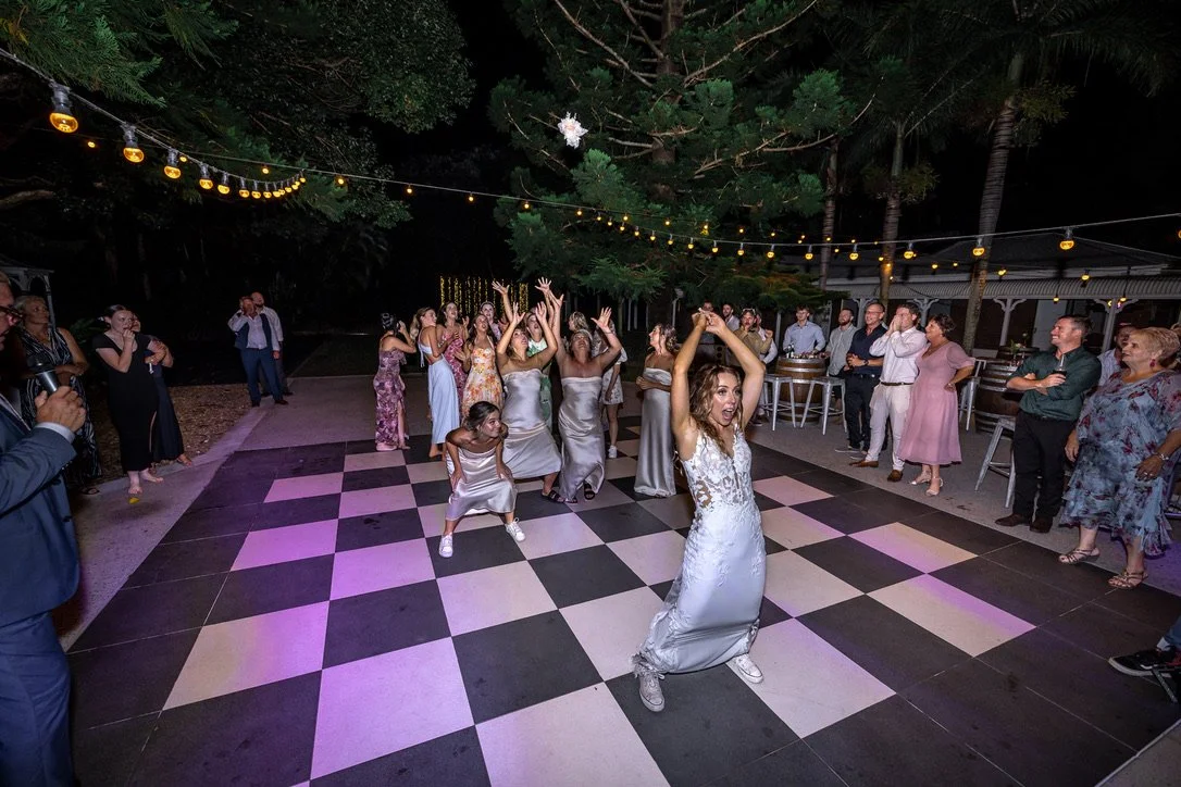 Guests celebrating on the dance floor under festoon lighting tossing of  the Bridal Bouquet wedding reception.