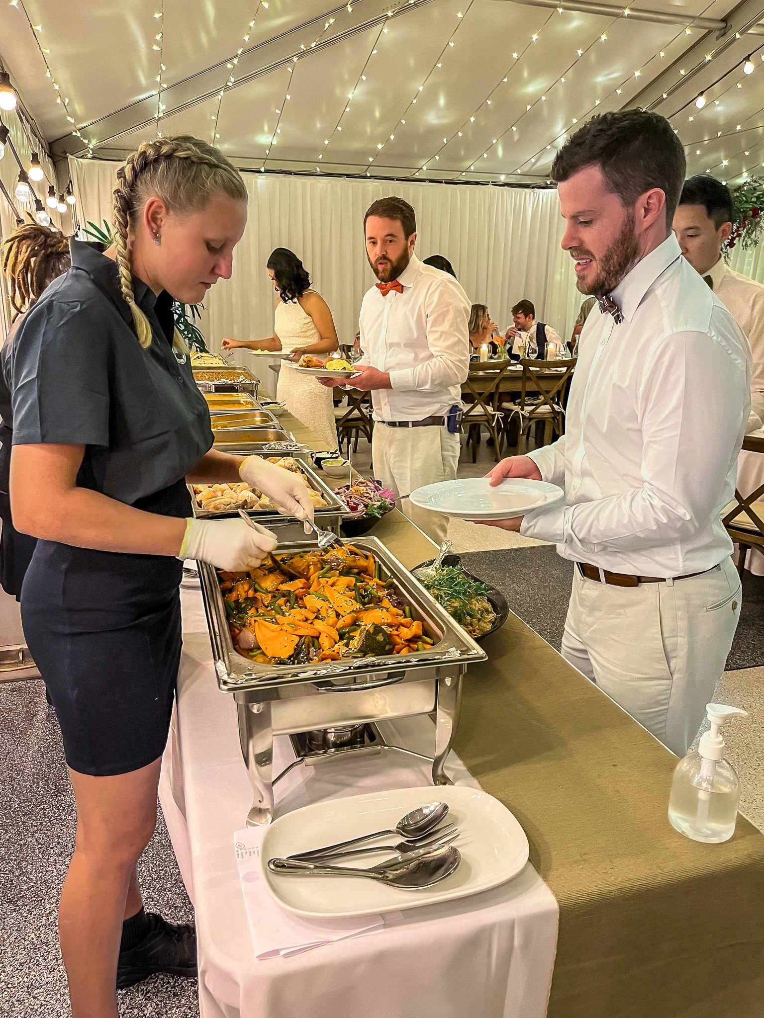 Guests being served from a hot buffet during a wedding reception in a garden marquee venue.