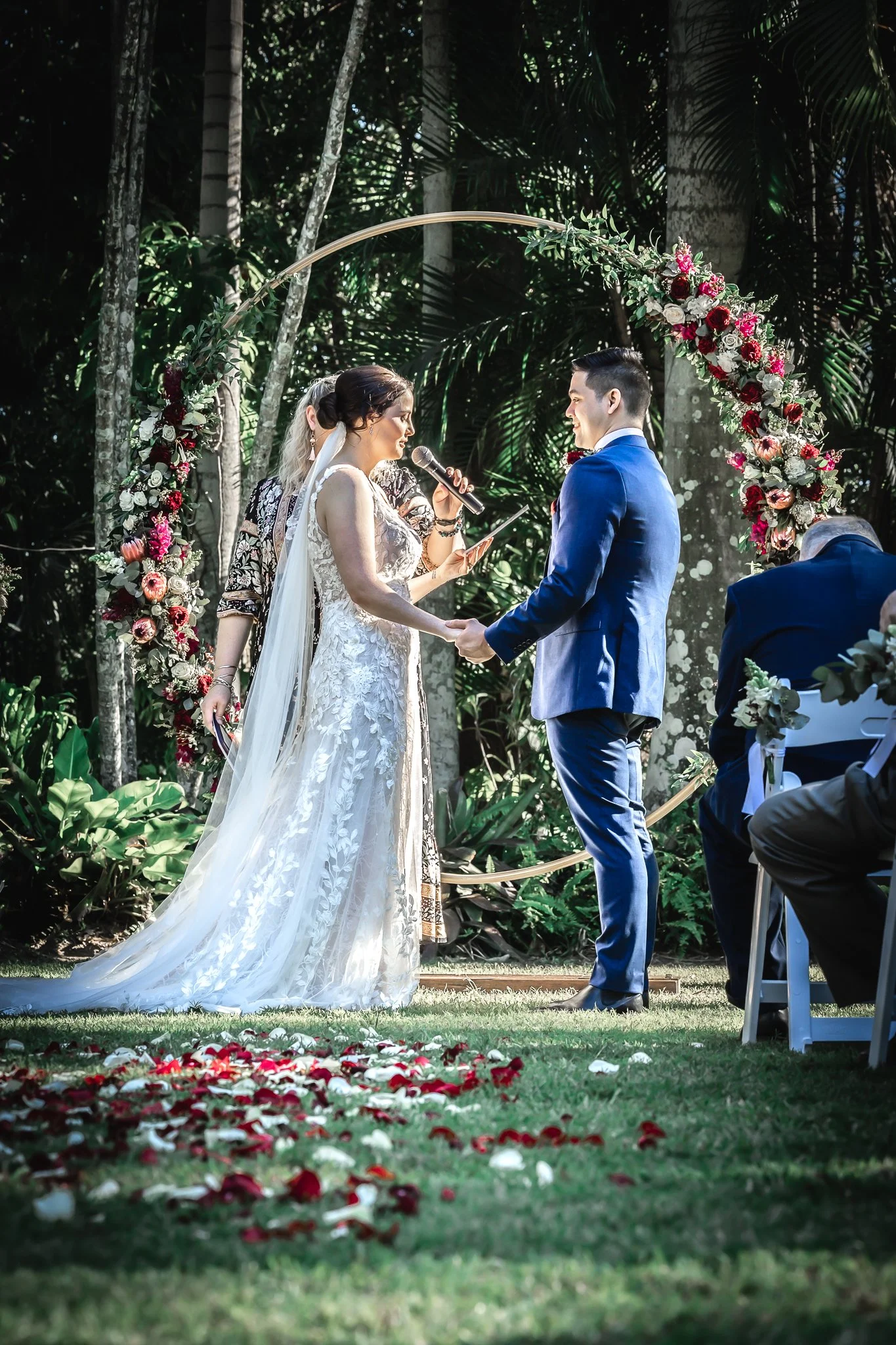 Outdoor wedding ceremony beneath a floral arbour set within a private garden venue in Queensland.